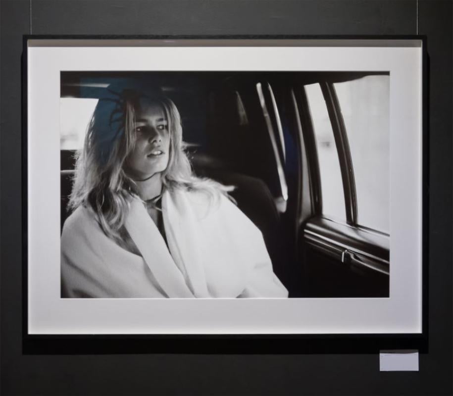 Claudia Schiffer - the young supermodel sitting in a car wearing a white coat - Photograph by Antoine Verglas