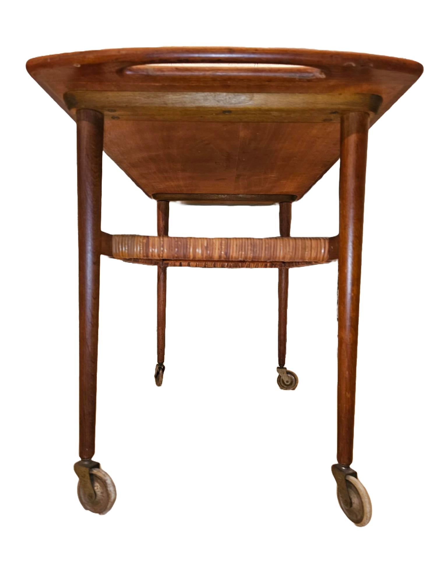 This beautiful piece is all original. It is in great condition - with the exception of the wheels which have been kept on to ensure authenticity and originality. This teak two-tiered cart has a woven rattan shelf at the bottom. This gorgeous tea