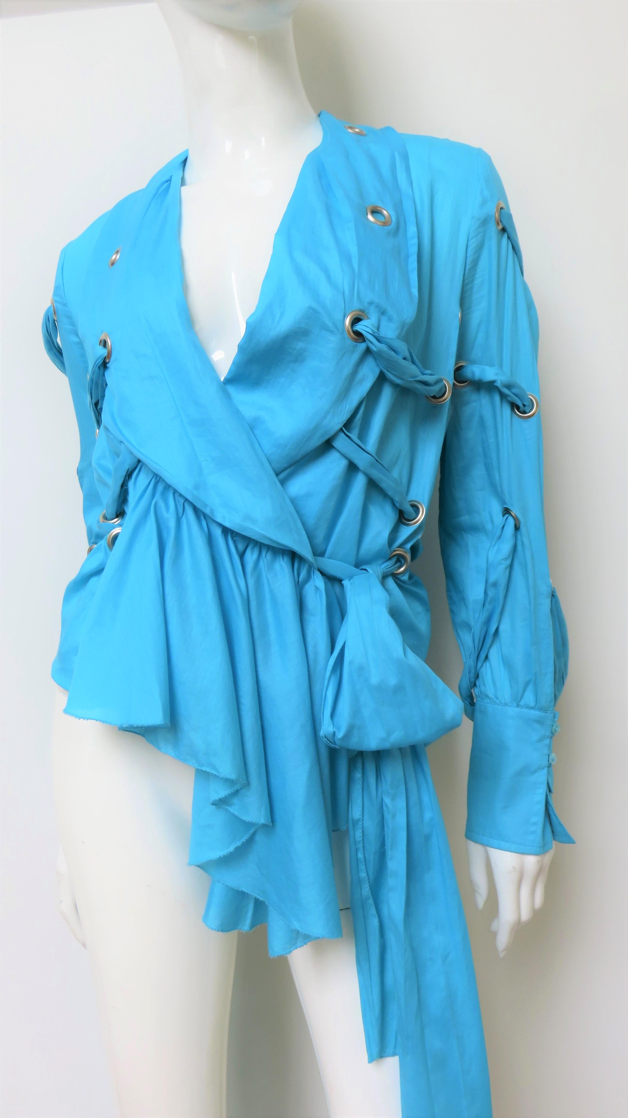 A fabulous bright blue fine cotton shirt, top, blouse by Antonio Berardi.  It has a shawl collar, matching mother of pearl button cuffs, and an asymmetrical hem longer in the front. The shirt has grommets in various locations and matching straps to