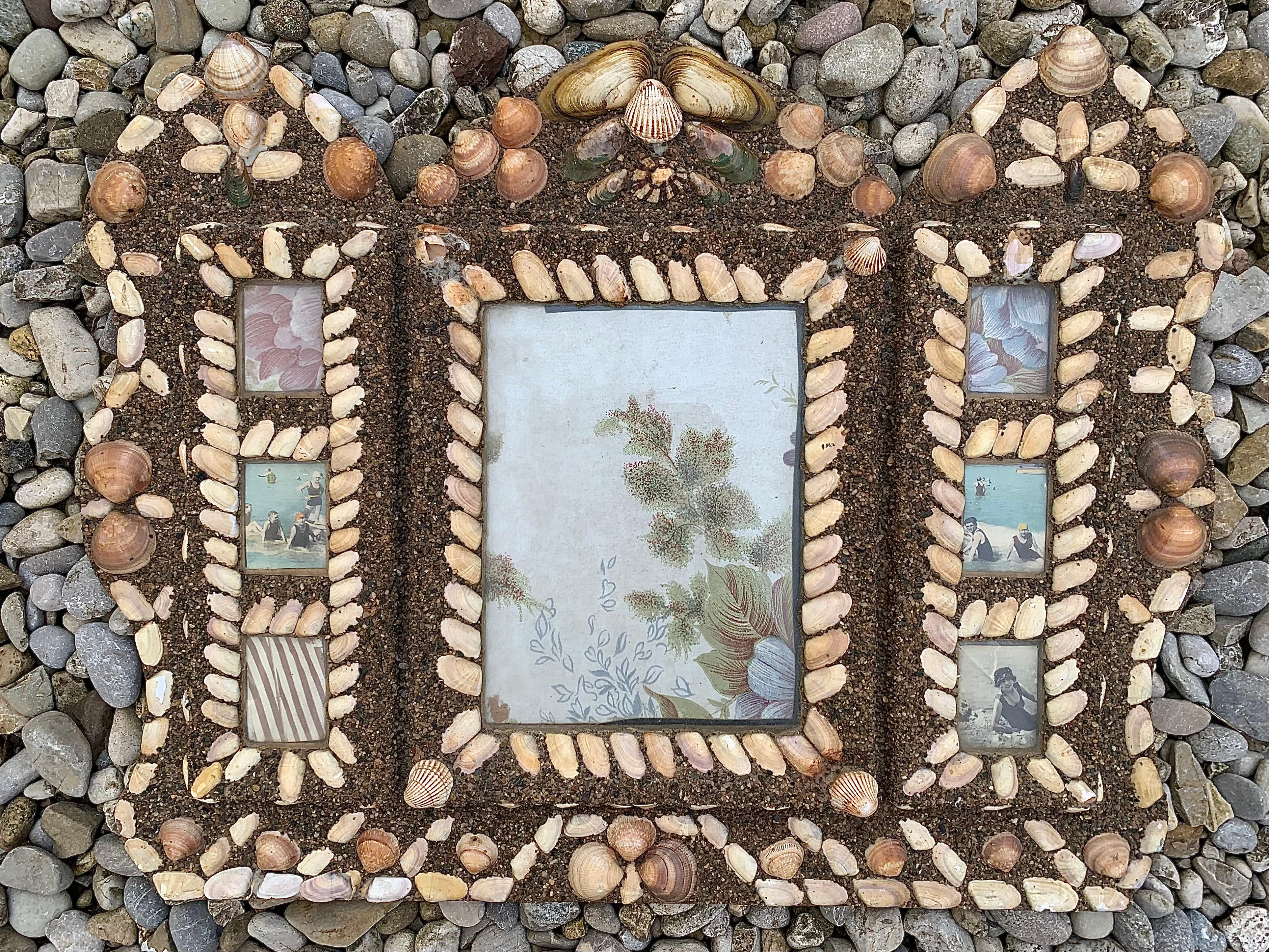 This highly unusual picture frame was handcrafted in 1920 ca, probably as a souvenir of a nice sea side summer holiday.. It is made out of cardboard and sand and decorated with a variety of shells. It has 7 compartments for pictures or
