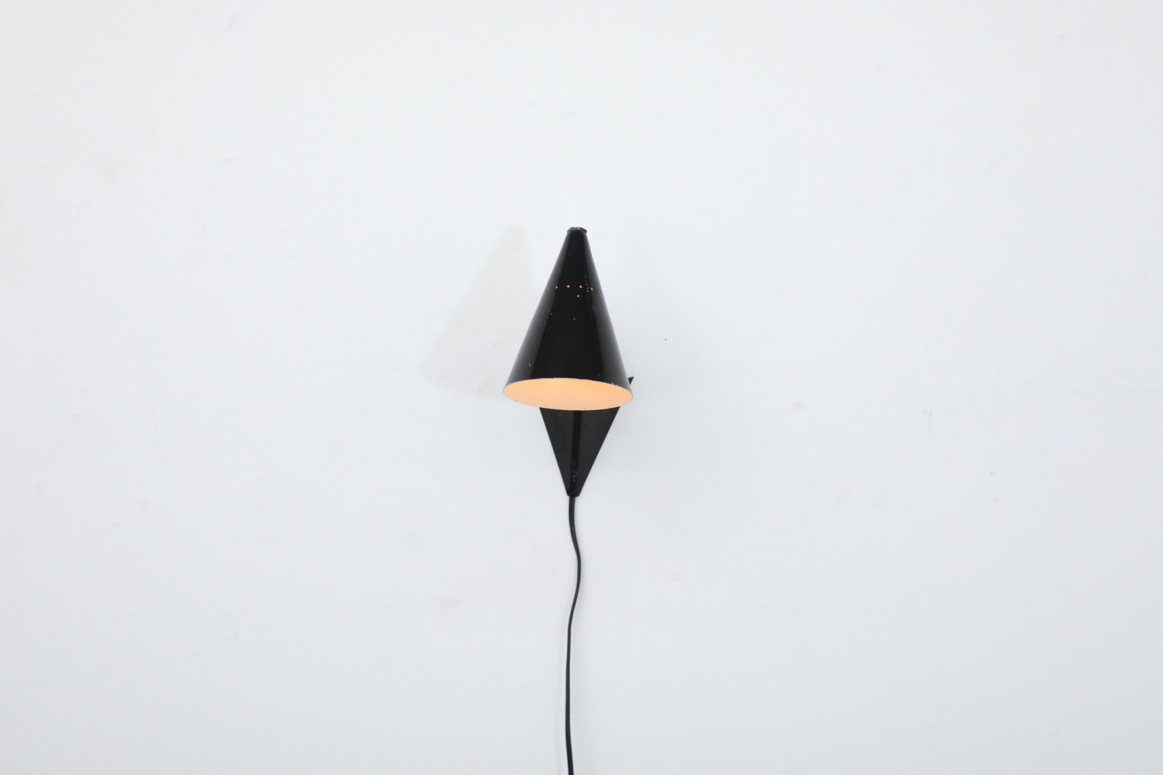 Mid-Century Anvia attributed black enameled wall mounted sconce with adjustable cone shaped shade, triangular base and brass stem. In original condition with visible wear, including chips, consistent with its age and use.