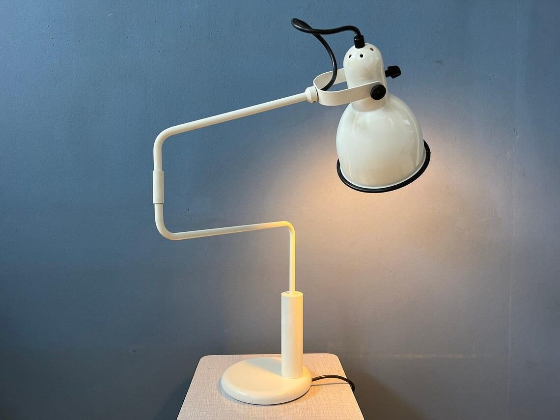 White Anvia 'elbow' desk lamp by Hoogervorst. This classic 'office' table lamp has a swing-arm that stretches all the way out. The lamps is made out of metal and has a white lacquer with black finish on the edge. The lamp has a switch on top of the