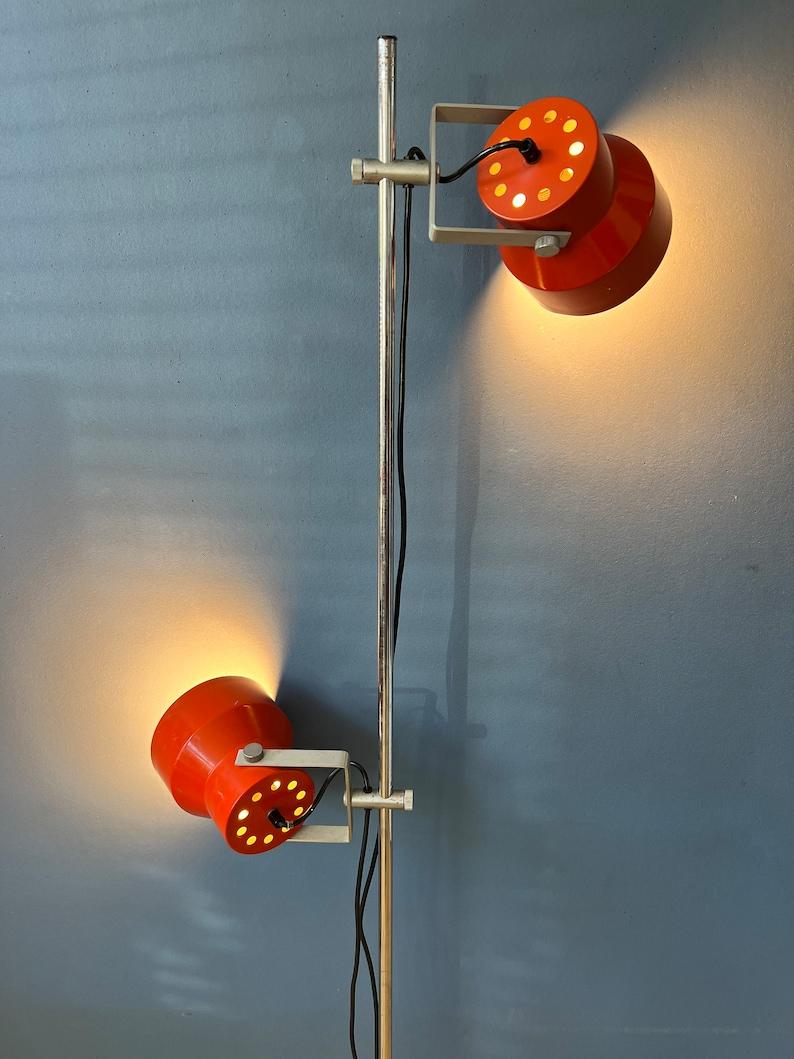 Mid century orange Anvia floor lamp with two adjustable shades. The two orange spots can be moved up and down the base and adjusted in any direction desirable. The lamp requires two E27 lightbulbs and currently has an EU-plug.

Additional