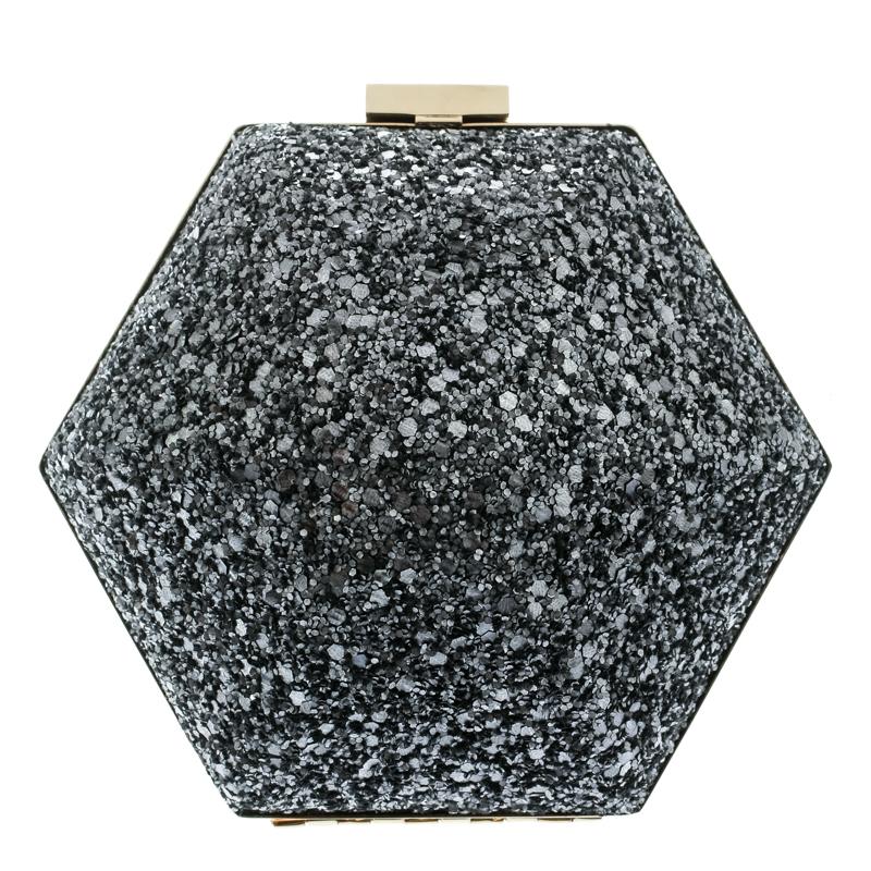 How breathtaking is this clutch by Anya Hindmarch! It is sparkly, well-crafted and overflowing with style. It brings a unique shape, grey glitter on the exterior, a gold-tone frame as well as chain and a suede interior. This creation will lift all