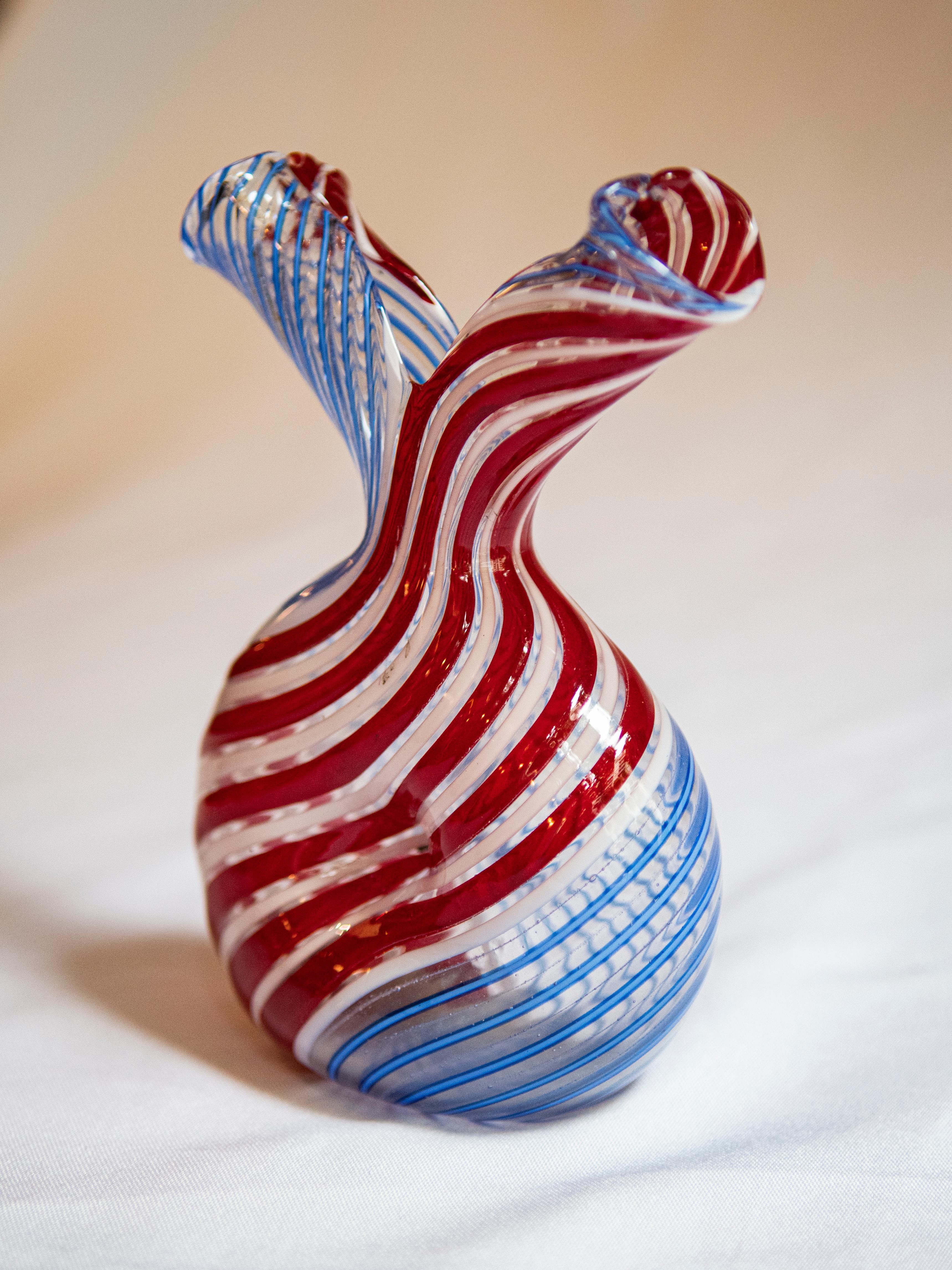 Transport yourself back to the vibrant era of the 1960s with this rare Italian handblown glass vase. Adorned with captivating light blue, white, and red stripes, it exudes the essence of retro charm and artistic flair. Each stripe is a testament to