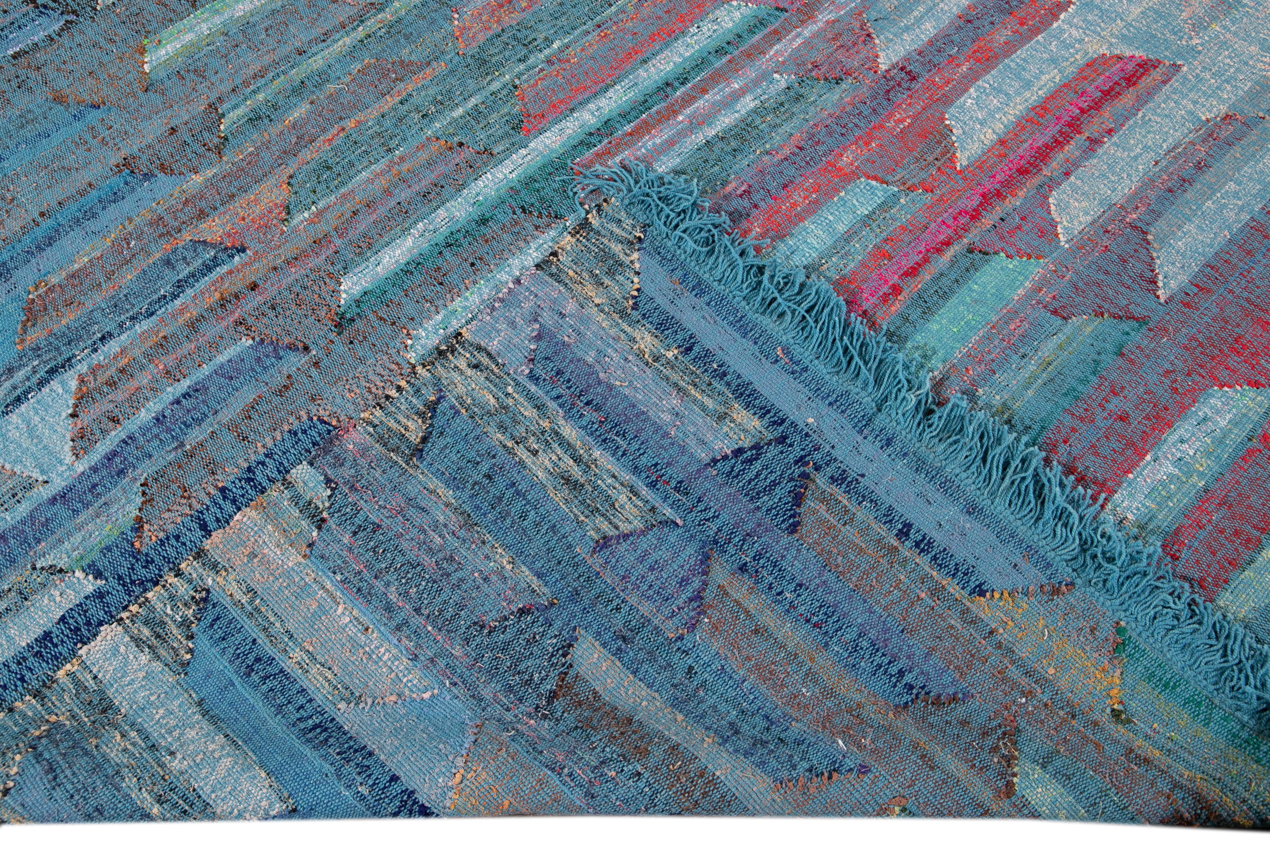 Beautiful modern Oversize Kilim flat-weave wool rug with a blue field. This piece of art has pink, green, and yellow accents in a gorgeous geometric abstract design.

This rug measures: 12'2