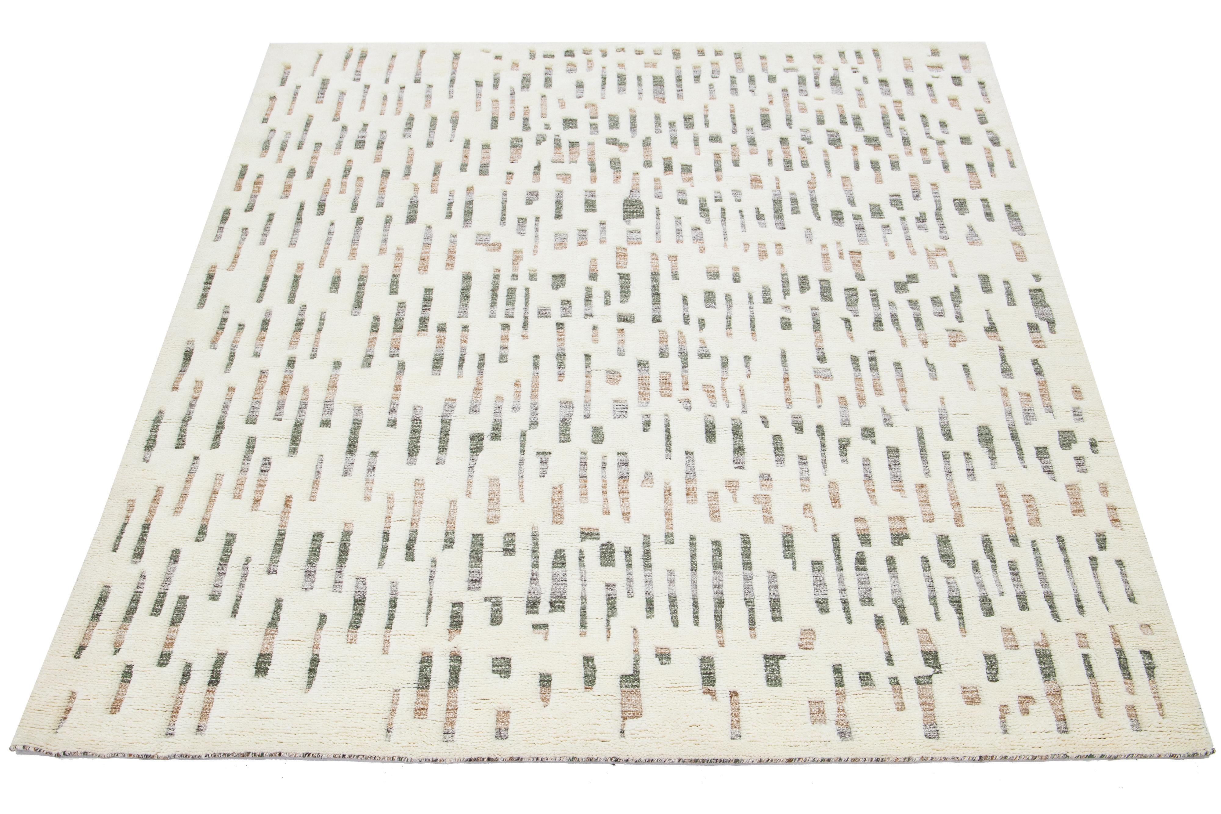 This Moroccan-style wool rug is hand-knotted and showcases a beautiful modern design with a natural ivory field. It features a stunning abstract pattern in green, gray, and brown.

This rug measures 8' x 10'.