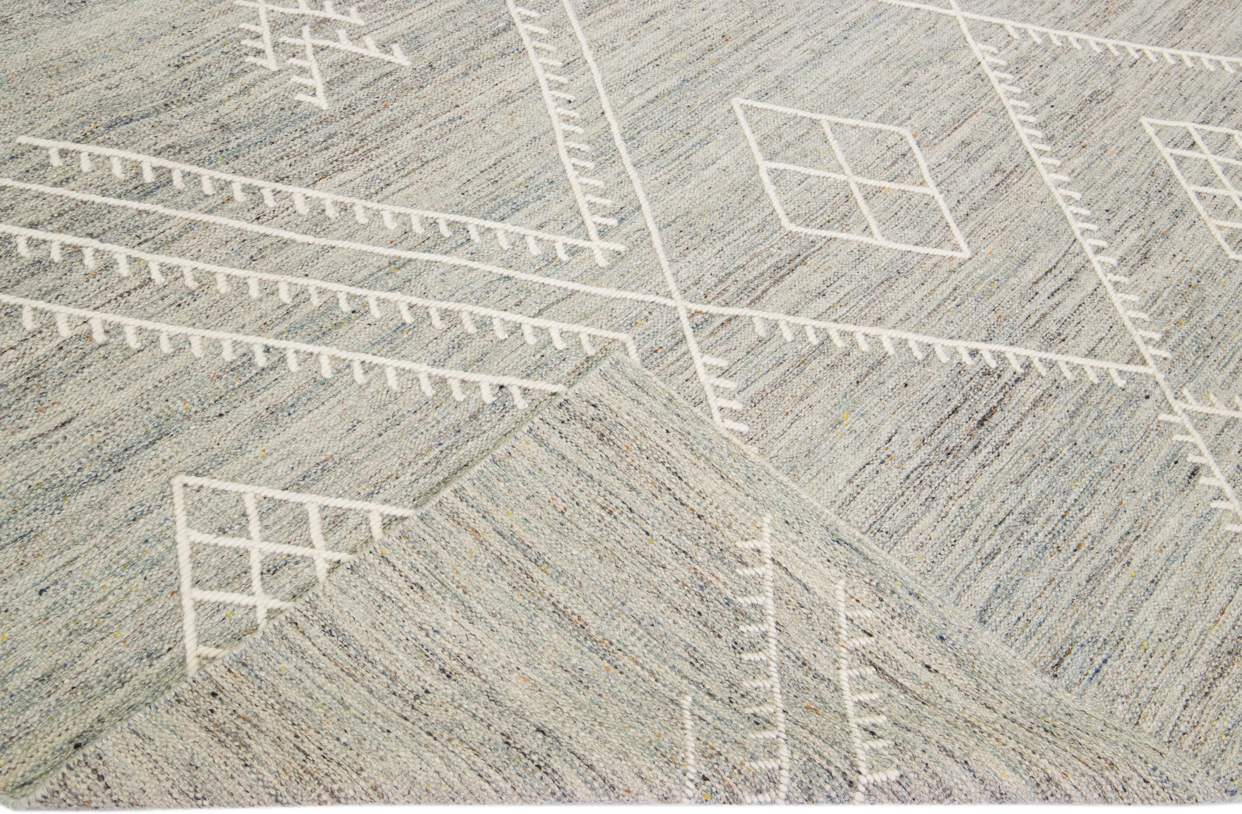 Magnifique tapis kilim en laine fait main avec un champ gris. Ce tapis moderne personnalisé à tissage plat, qui fait partie de notre collection Nantucket, présente des accents ivoires et un magnifique motif géométrique côtier.

Ce tapis mesure :