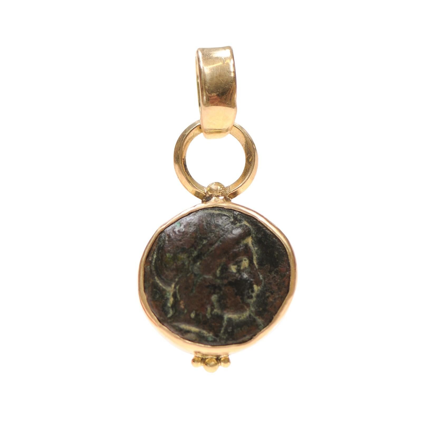 Eine antike griechische Bronzemünze als Anhänger in 18-karätigem Gold eingefasst. Diese Münze wurde CIRCA im 3. Jahrhundert v. Chr. geprägt. Auf der Vorderseite ist das Porträt des Gottes Apollo und auf der Rückseite ein Musikinstrument abgebildet.