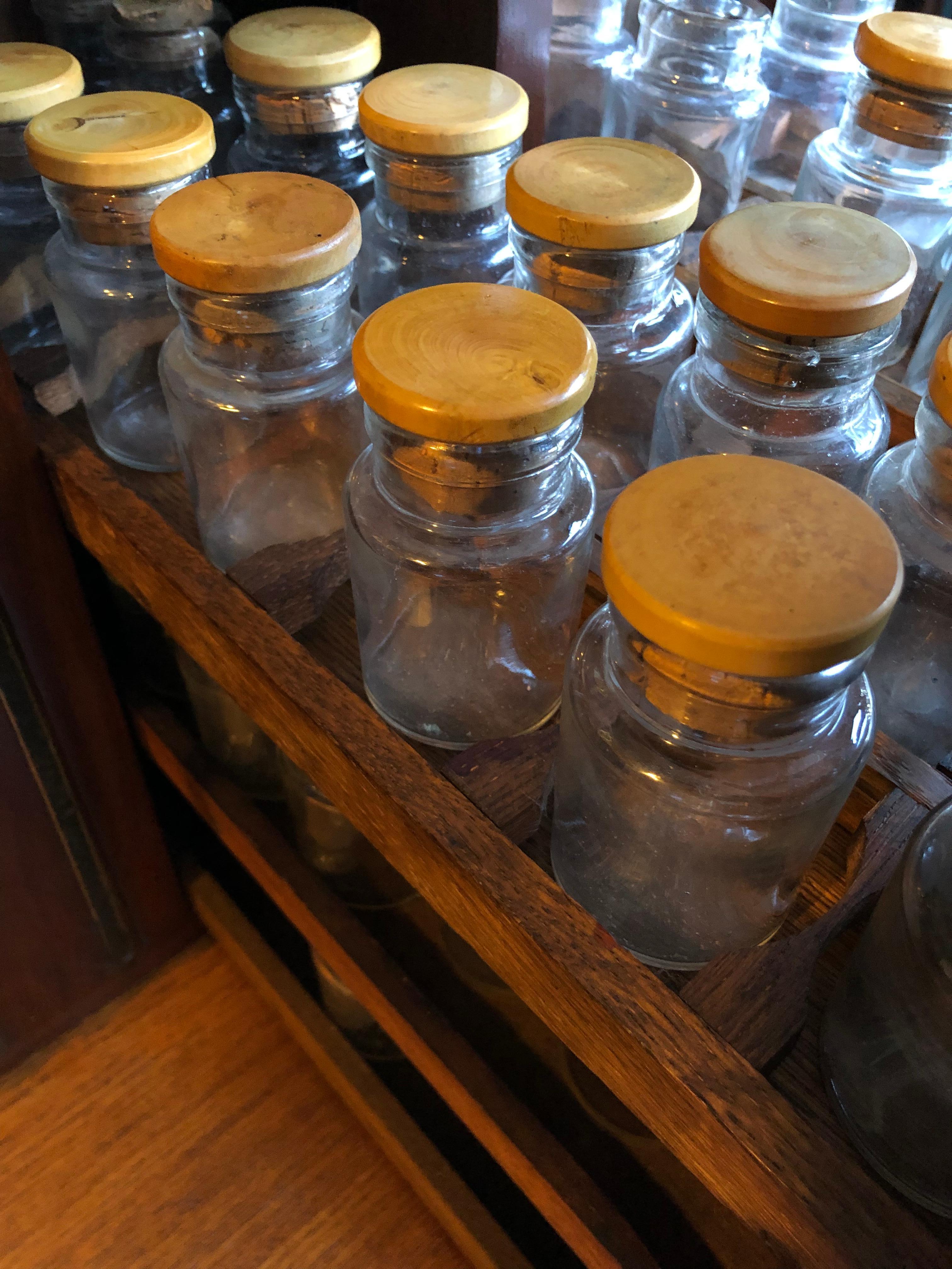 A highly unusual hardwood apothecary cabinet from the early 20th century. Unique vertical drawer construction with shelves and adjustable holders containing original 113 assorted glass bottles. Some with cork and turned wood stoppers. A substantial