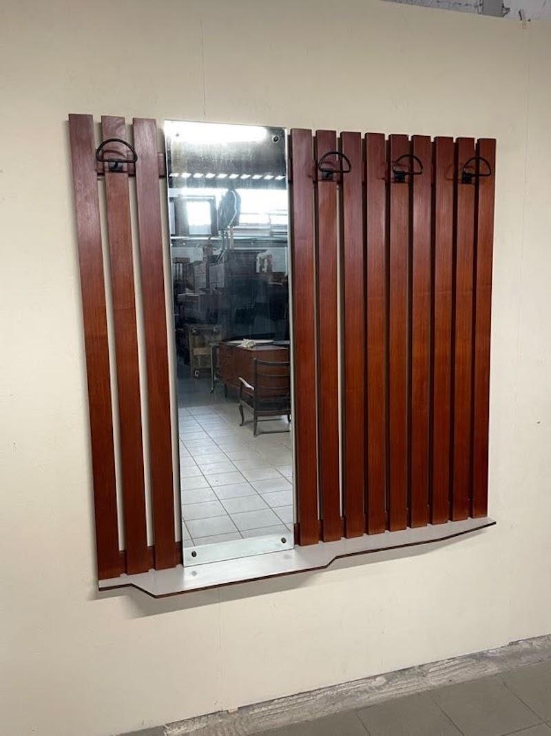 Appendiabiti da muro anni '60 con rastrelliera in legno di teak e appendini in metallo.

Al centro è posizionato uno specchio ancora originale e alla base mensola sagomata in formica dell'epoca.

Condizioni ottime e perfetto per un ingresso o una