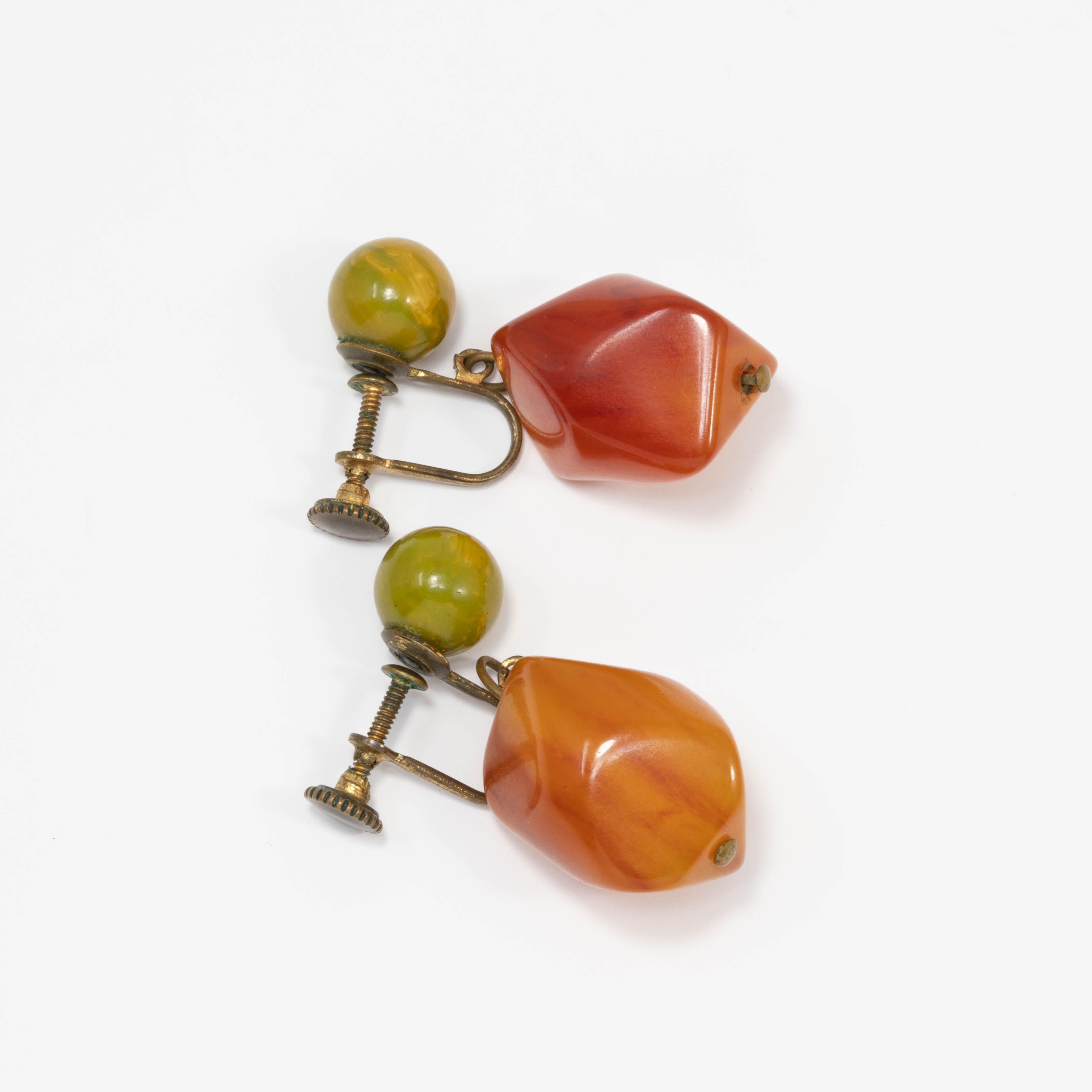 A pair of vintage bakelite dangle earrings. Features an apple green bakelite bead and a dangling amber orange bakelite accent for a complimentary contrast. Vintage brass-tone screw back closure.