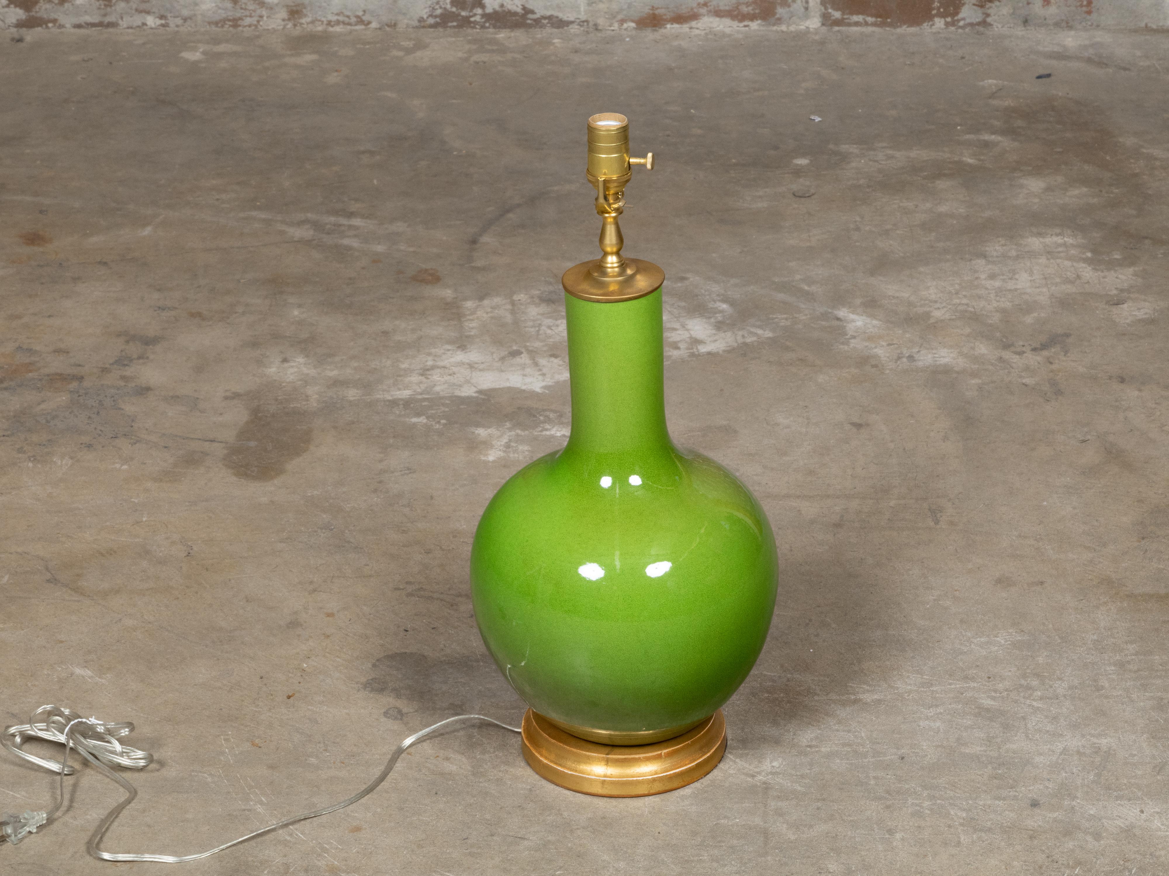 Un vase lumineux en porcelaine vert pomme, maintenant configuré comme une lampe de table à prise unique, monté sur une base circulaire en bois doré. La forme lisse et gracieuse du vase est rehaussée par sa riche glaçure, d'un vert vif à la fois