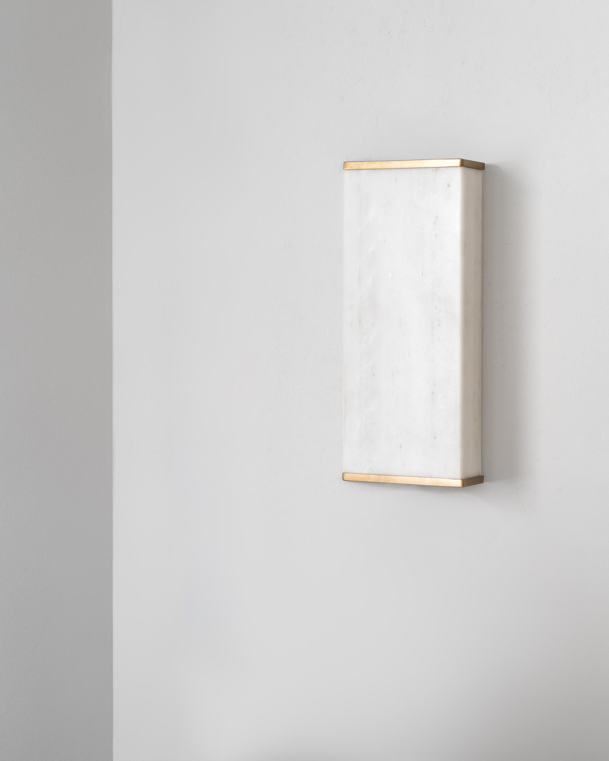Appleak wall light highlights the translucency of marble and its unique crystalline quality. 

It consists of a seamless volume and a bronze frame. With a triangular, off-centred geometry, it features an elegant but also sophisticated