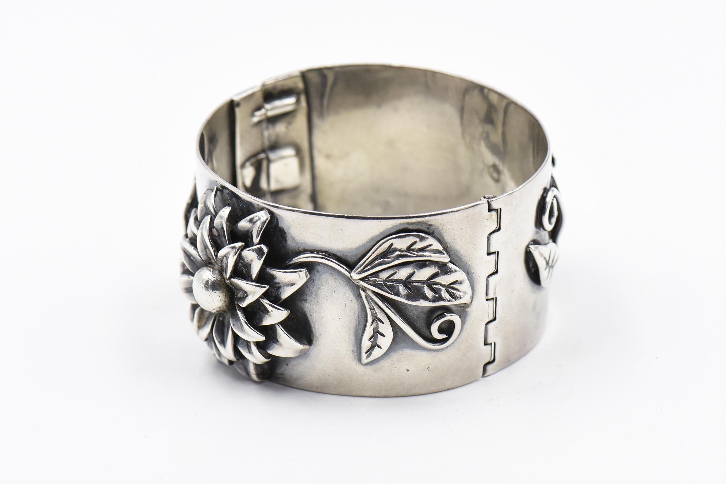 Handwrought sterling silver flower bangle by Heidi. Open by pulling open tab then lifting lever.  It has a safety chain also.  Marked sterling and signed by Heidi

Interior circumference 6.5