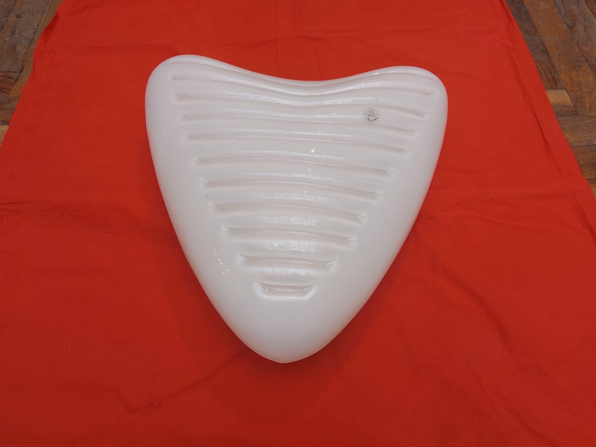 Applique a forma di cuore in vetro opalino bianco di Murano con modanature orizzontali. Si suppone, per la bella qualità, sia riconducibile ad un'importante produzione, forse di Venini. Ancora incollato all'oggetto è il bollino con l'indicazione