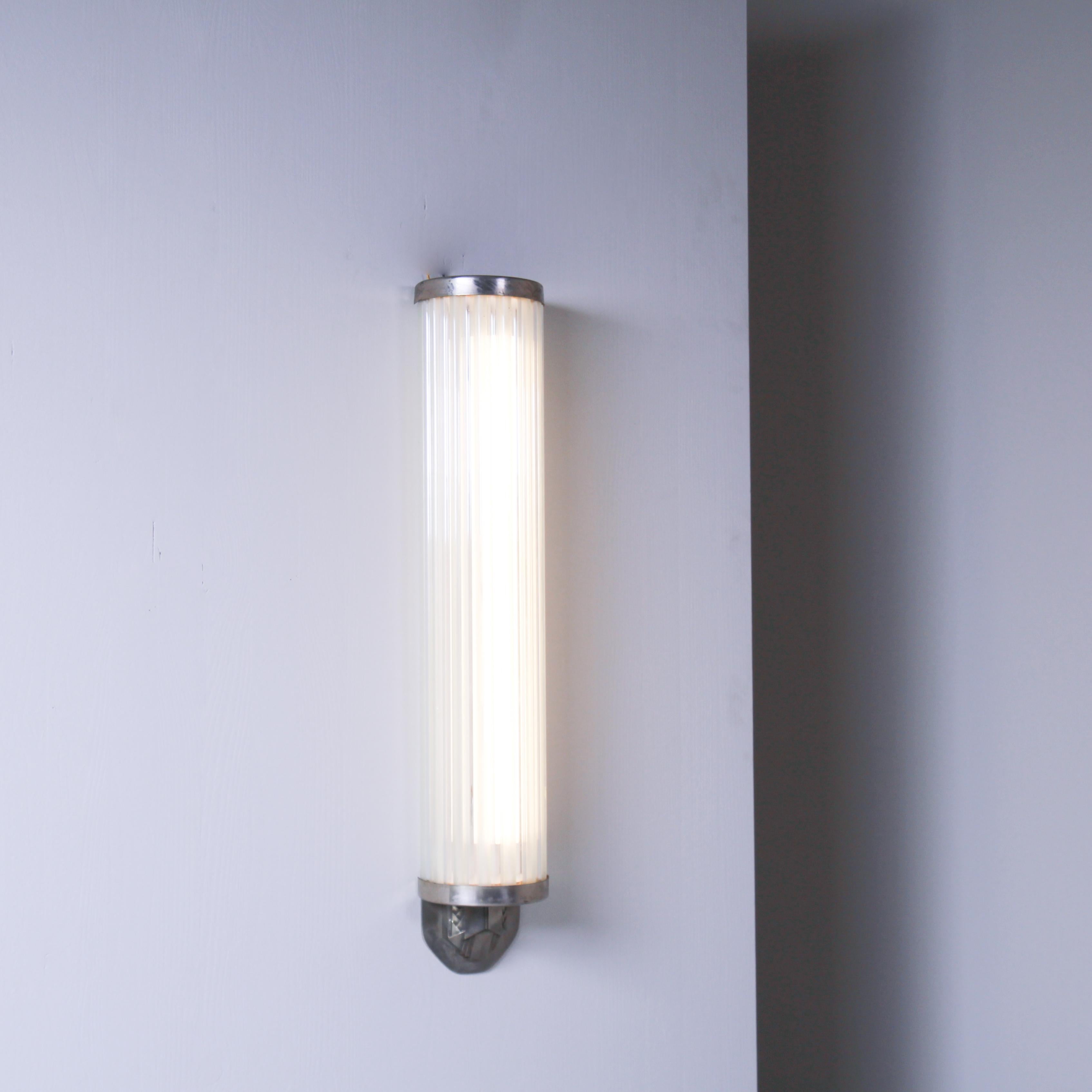 This original wall sconce from the 1930s embodies the Art Deco style with its combination of materials and elegant geometric shapes. The frame is made of metal, characterized by clean lines and refined design typical of the period. The distinctive