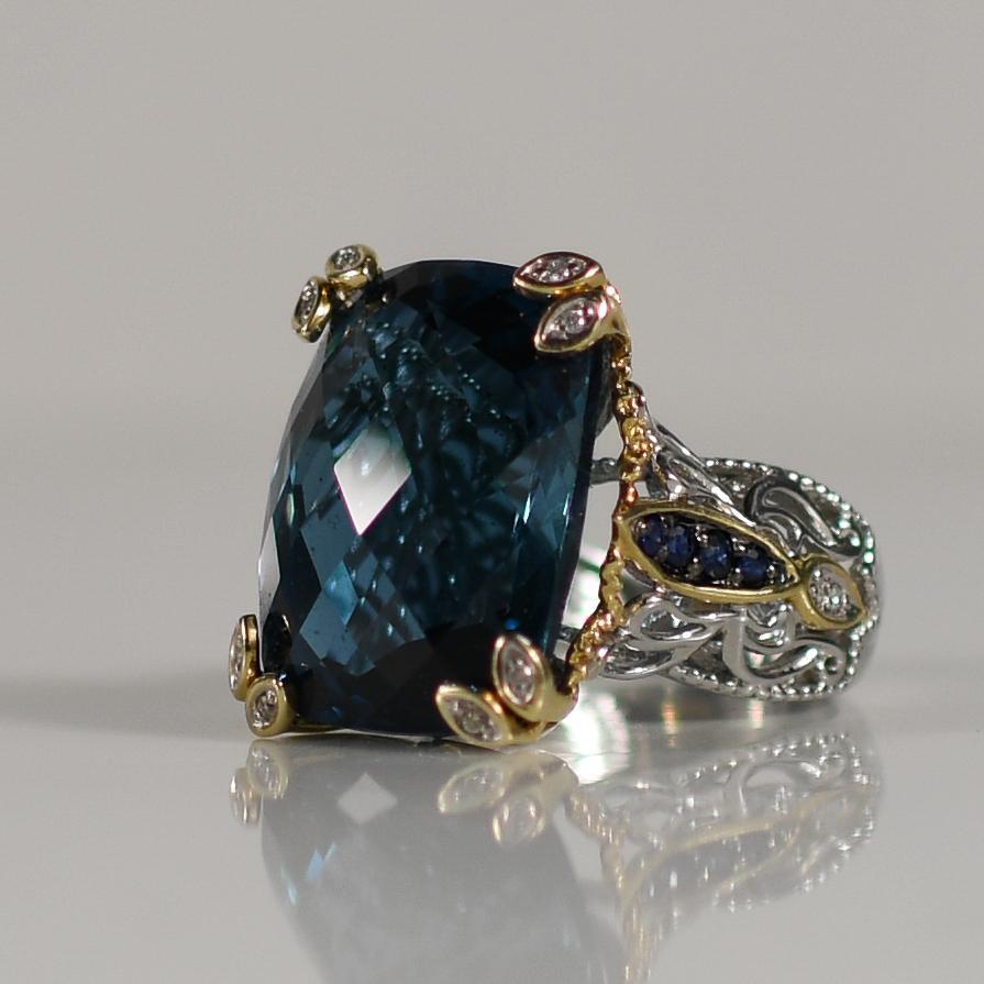 This breathtaking statement ring features an approximately 40-carat blue topaz, radiating a captivating azure hue. The striking gemstone is set in 14k white gold, secured by 14k yellow gold prongs that add a touch of warmth and contrast. Sapphire