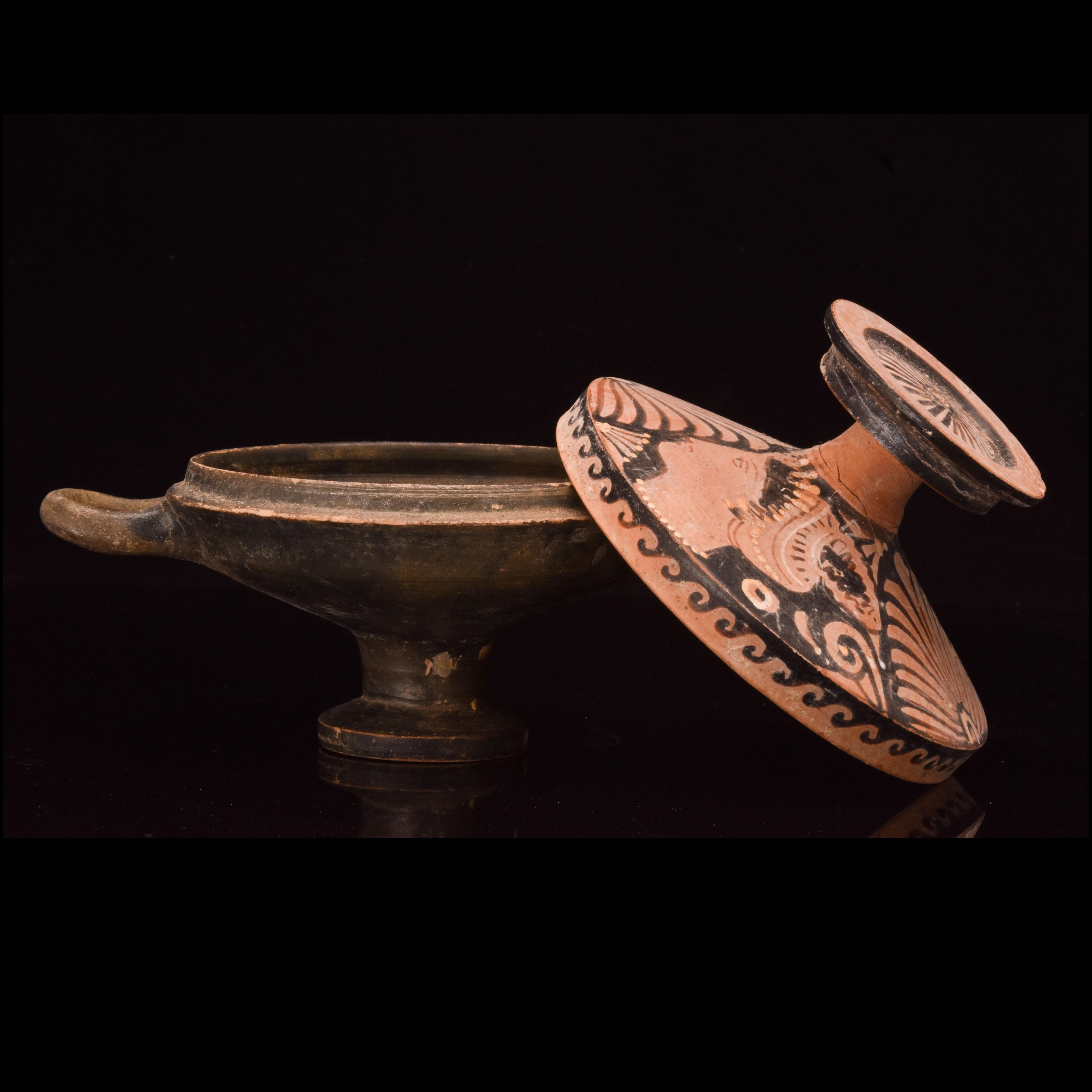 An Apulian lekanis comprised of two distinct components. The lower portion features a footed bowl adorned with a sleek black glaze, providing an elegant foundation for the vessel. Two opposing horizontal handles, meticulously crafted, facilitate