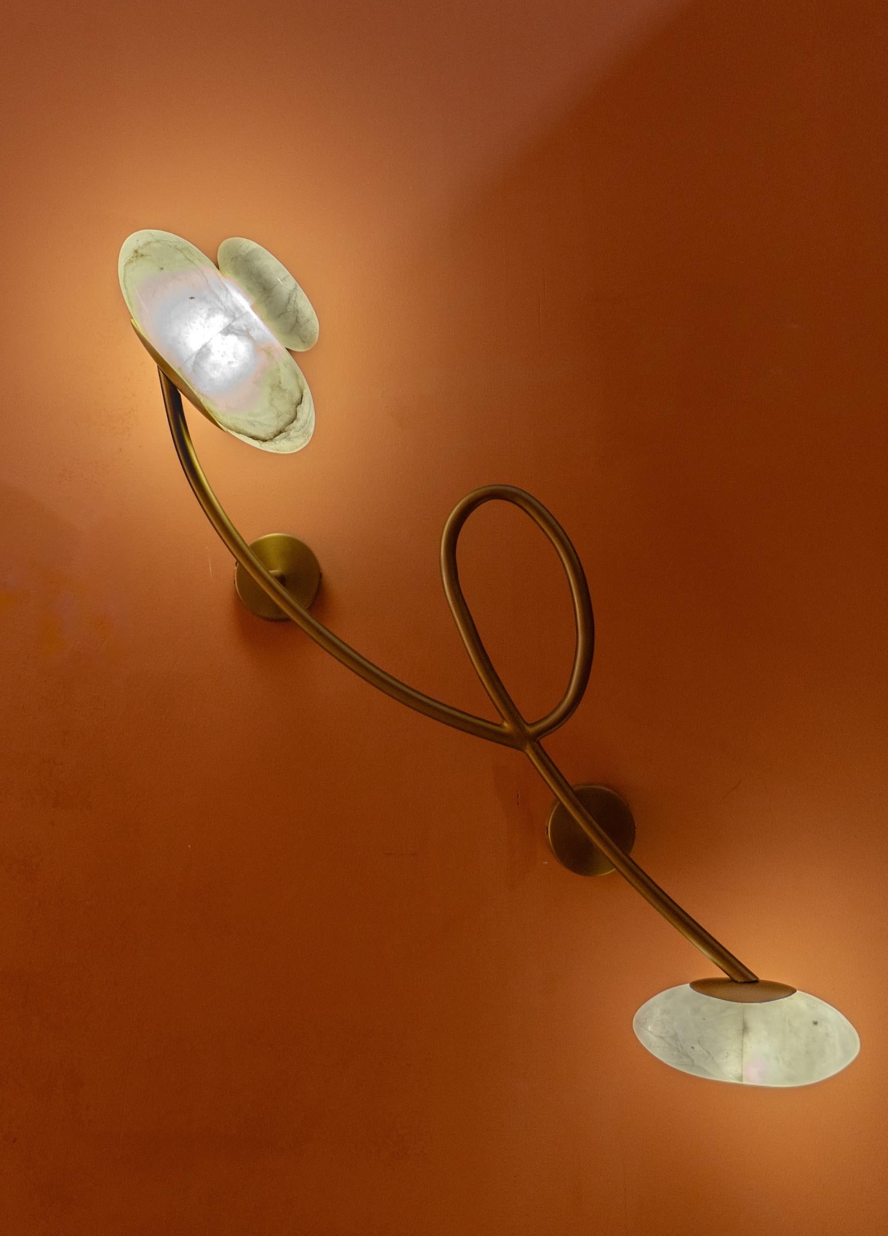 Este aplique escultural es una sorprendente fusión de arte y funcionalidad, diseñada para crear un ambiente cálido y acogedor. Elaborada con una estructura fluida y orgánica en acabado latón, la pieza presenta unos brazos graciosamente curvados que