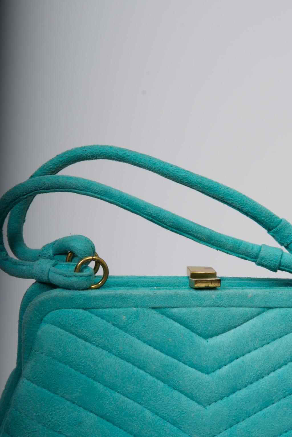 A unique find, this vintage handbag cannot fail to make you smile. Constructed of aqua suede that is channel-stitched in an inverted V-pattern, it is composed of two separate and conjoined purses, each with its own matching handle and simple gold