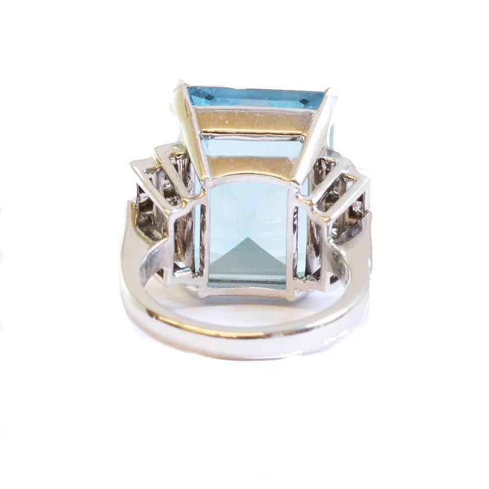 A cocktail ring set with a large emerald cut aquamarine, flanked by two rows of diamonds. Mounted in platinum. English, circa 1930.
