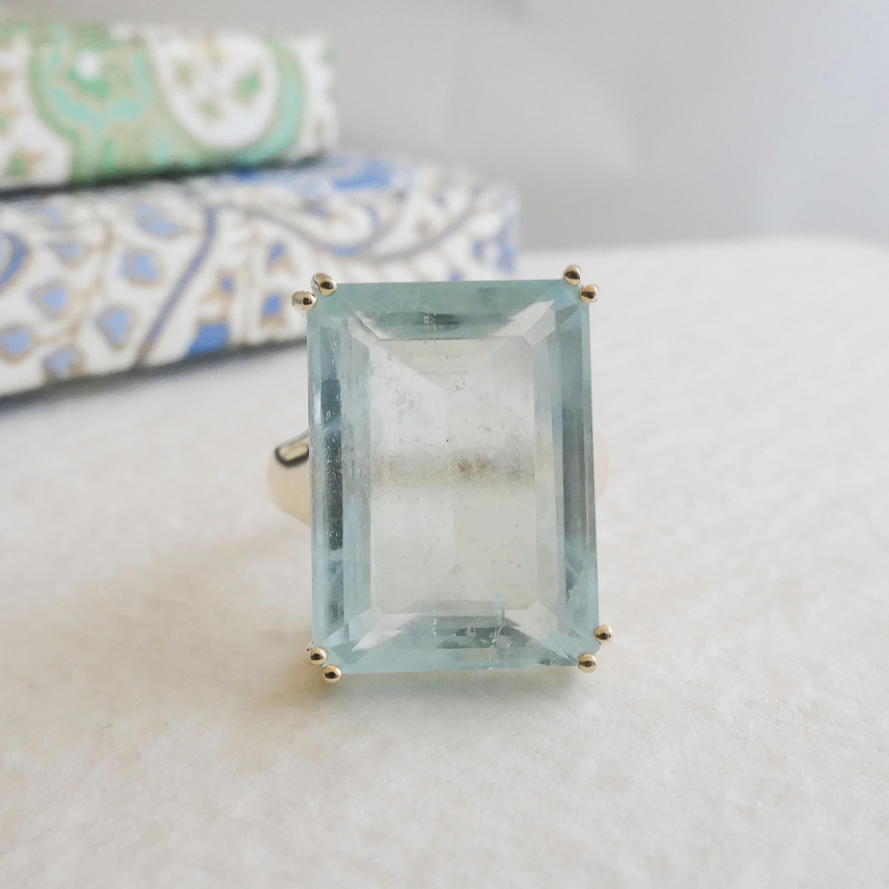 Faites preuve d'audace avec cette bague exquise ornée d'une magnifique aigue-marine de 22 carats. L'aigue-marine de 15 x 20 mm à taille rectangulaire est méticuleusement sertie dans un anneau en or jaune 14 carats, mettant en valeur sa teinte bleu