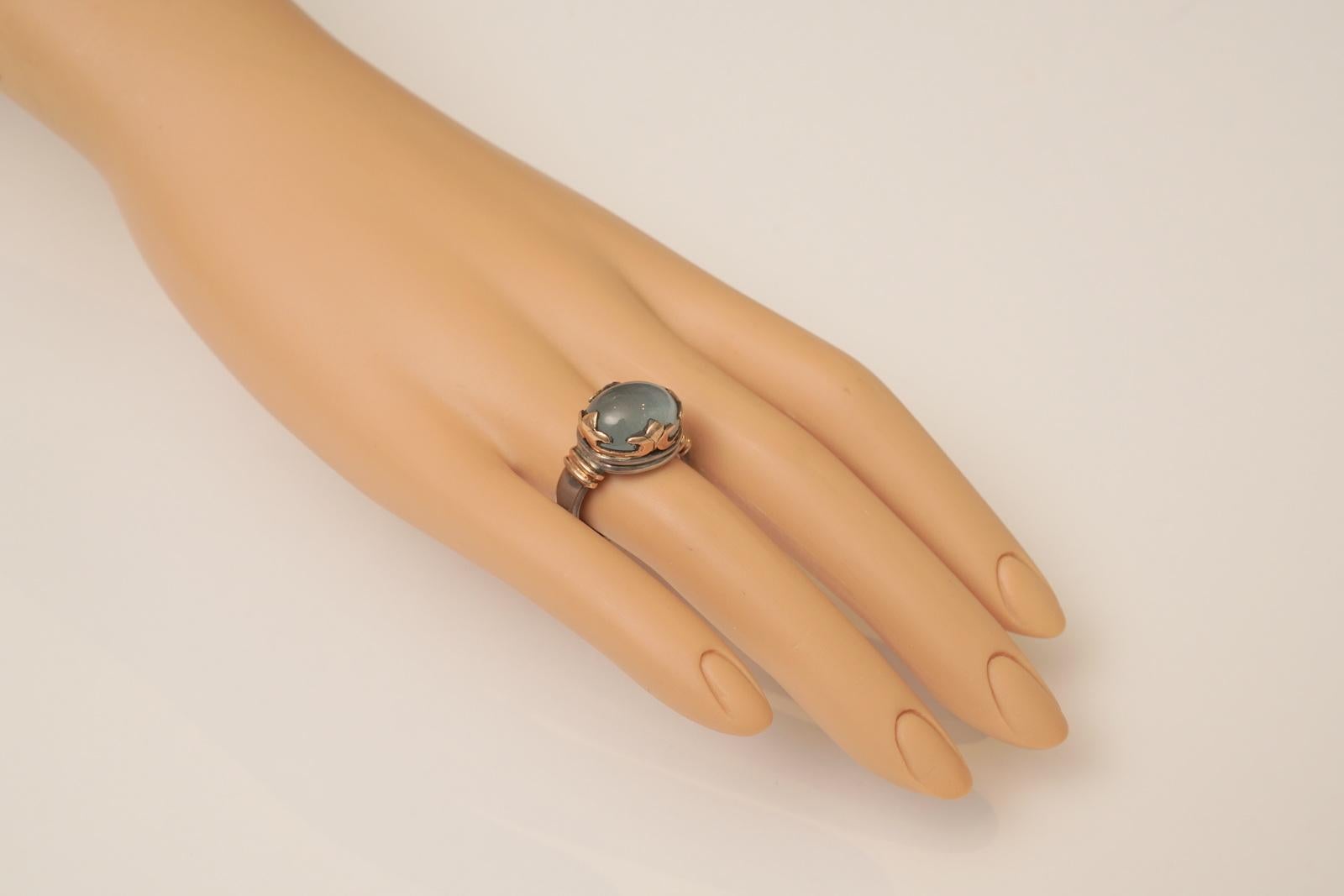 Classic with a twist, a large cabochon aquamarine set with a weighted (as in not plated) 18K gold Fleur de Lis bezel and same gold accents along the top. Otherwise, the band is in sterling silver. Ring size is 6.75