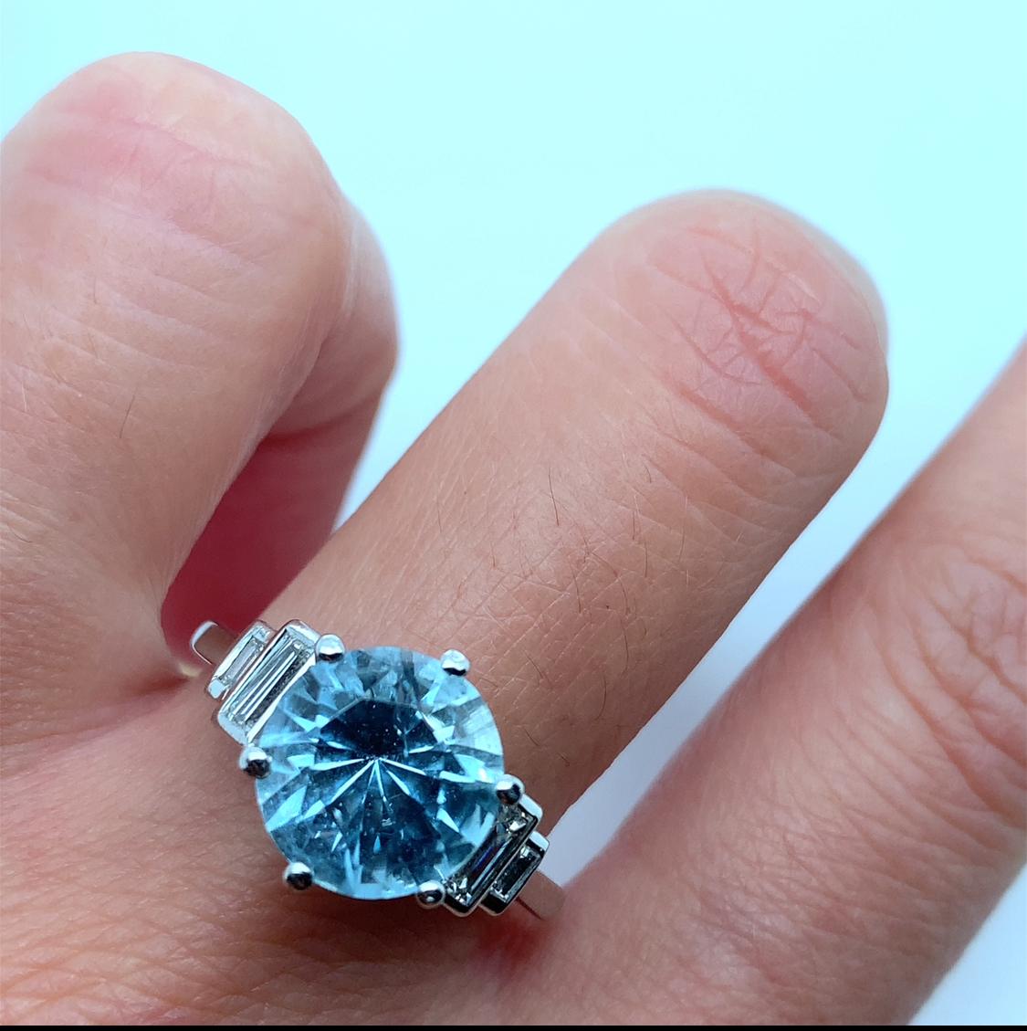 Cette superbe bague de fiançailles aigue-marine et diamant baguette trilogie ou bague de cocktail est une véritable œuvre d'art. La bague est fabriquée en platine, avec un magnifique sertissage de diamants taillés en escalier qui rehausse l'éclat