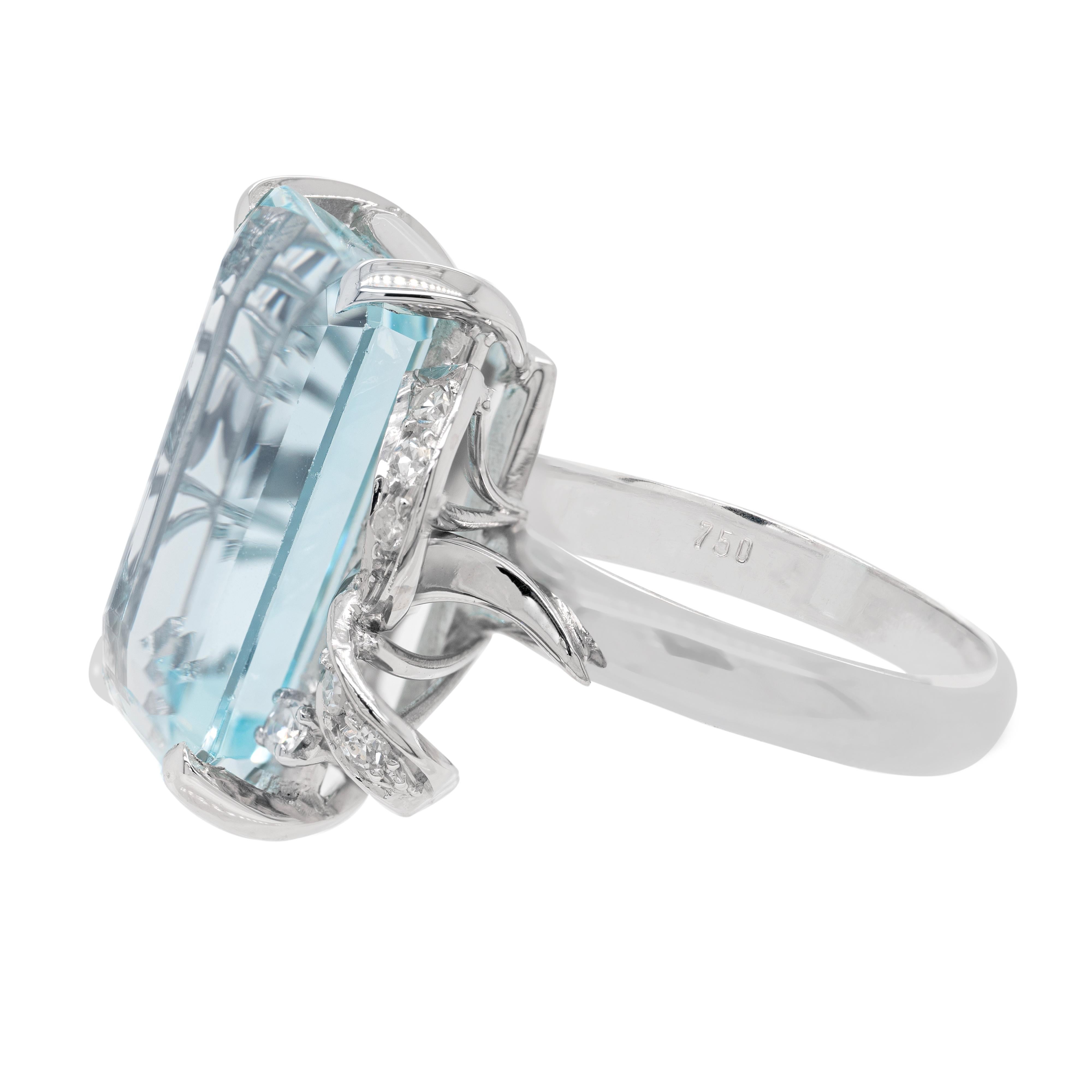 This wonderful 18 carat white gold dress ring features an emerald cut aquamarine weighing approximately 13.00 carats, mounted in a four claw, open back setting. The impressive stone is accompanied by two white gold ribbons on either side, each