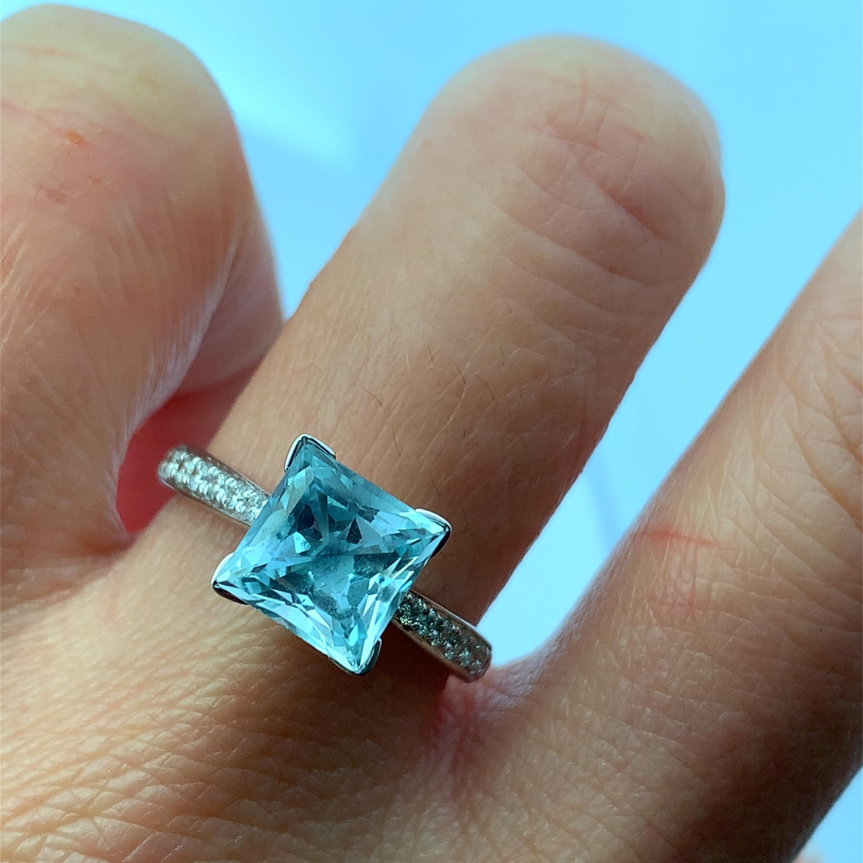 Entdecken Sie die Anziehungskraft dieses atemberaubenden blauen Aquamarins von 2,10 Karat, der mit seinem fesselnden Quadratschliff bei jeder Bewegung funkelt. Das zarte Band ist mit schimmernden Diamanten 0,60ct F VS1 verziert und eignet sich