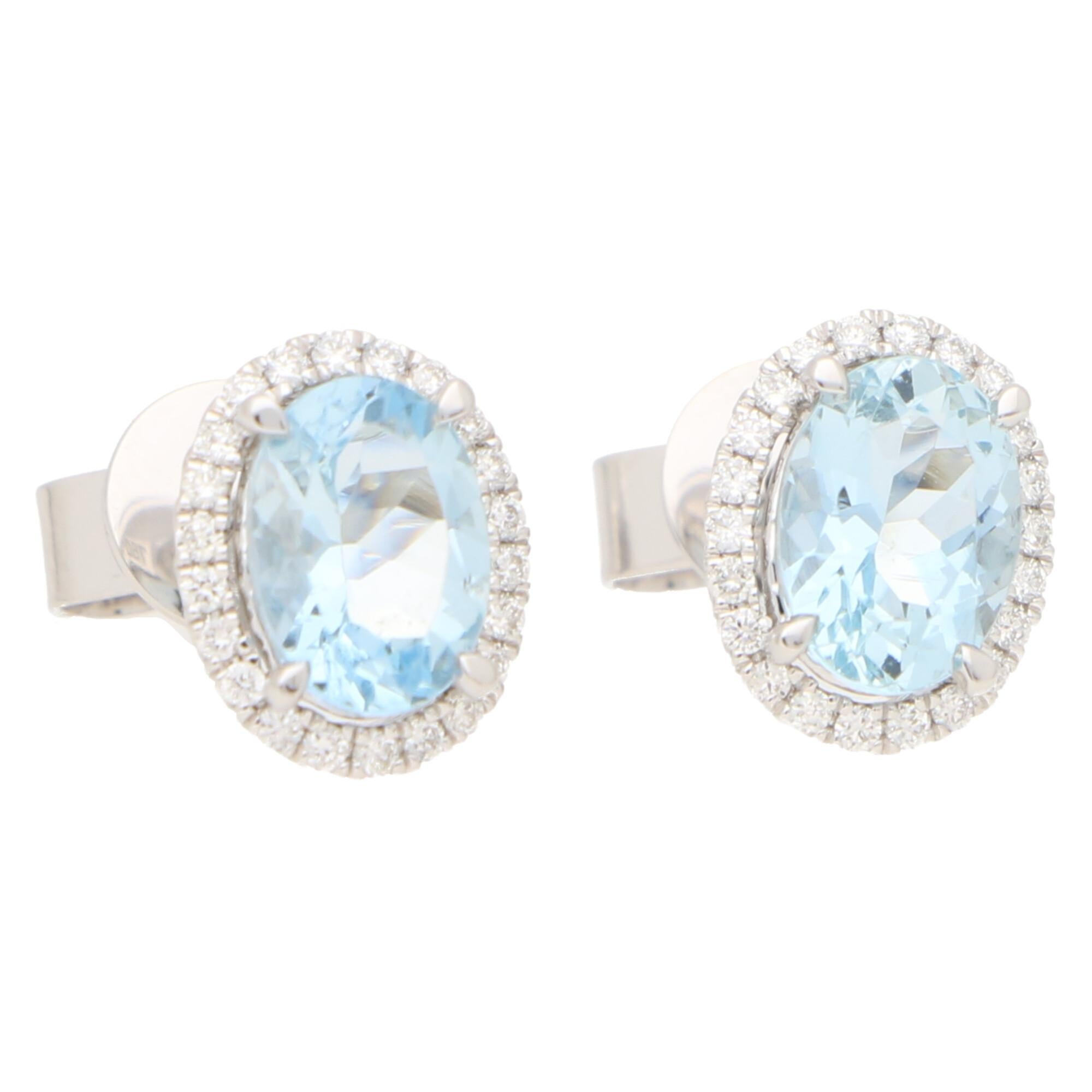 A lovely pair of aquamarine and diamond oval halo earrings set in 18k white gold.

Each earring centrally features a beautiful blue colored oval shaped aquamarine surrounded by a halo of 22 round brilliant-cut diamonds. All of the stones are set to