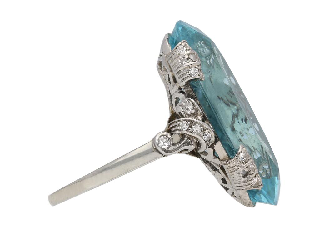 Anello con acquamarina e diamanti. Al centro è incastonata un'acquamarina naturale ovale mista taglio a forbice in una montatura a griffe aperta sul retro con un peso approssimativo di 12,00 carati, affiancata da ventisei diamanti rotondi taglio a