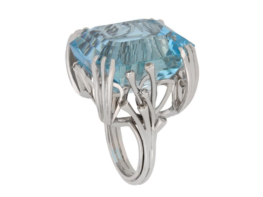 Aquamarine and diamond solitaire ring. Set to center with an octagonal emerald cut natural aquamarine in open back claw settings with an approximate weight of 38.65 carats, flanked by twelve round eight cut diamonds in closed back rubover settings