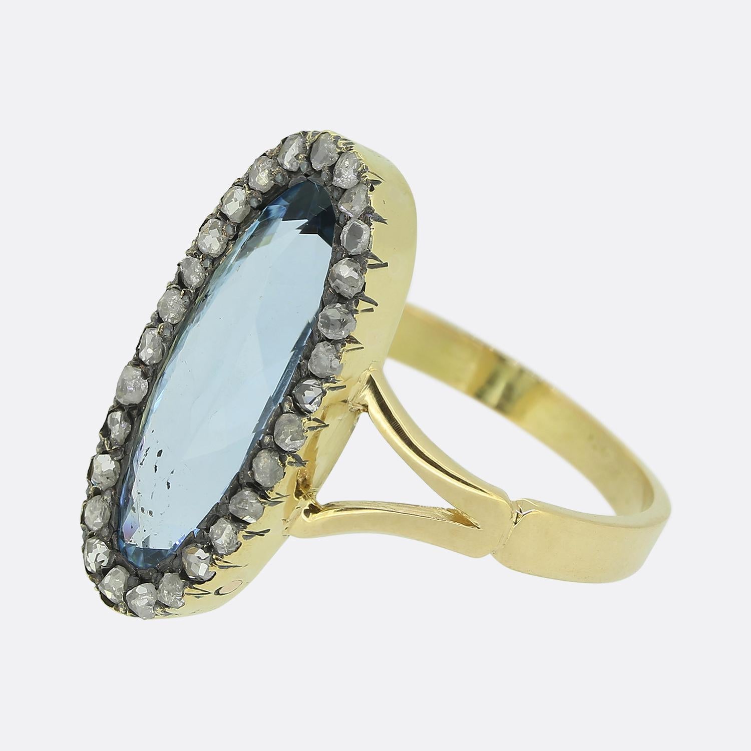 Here we have an elegant dress ring. This vintage piece focally features an elongated oval-faceted aquamarine at the centre of the face, showcasing a captivating blue hue. Surrounding this primary stone around the outer edge is a single line of