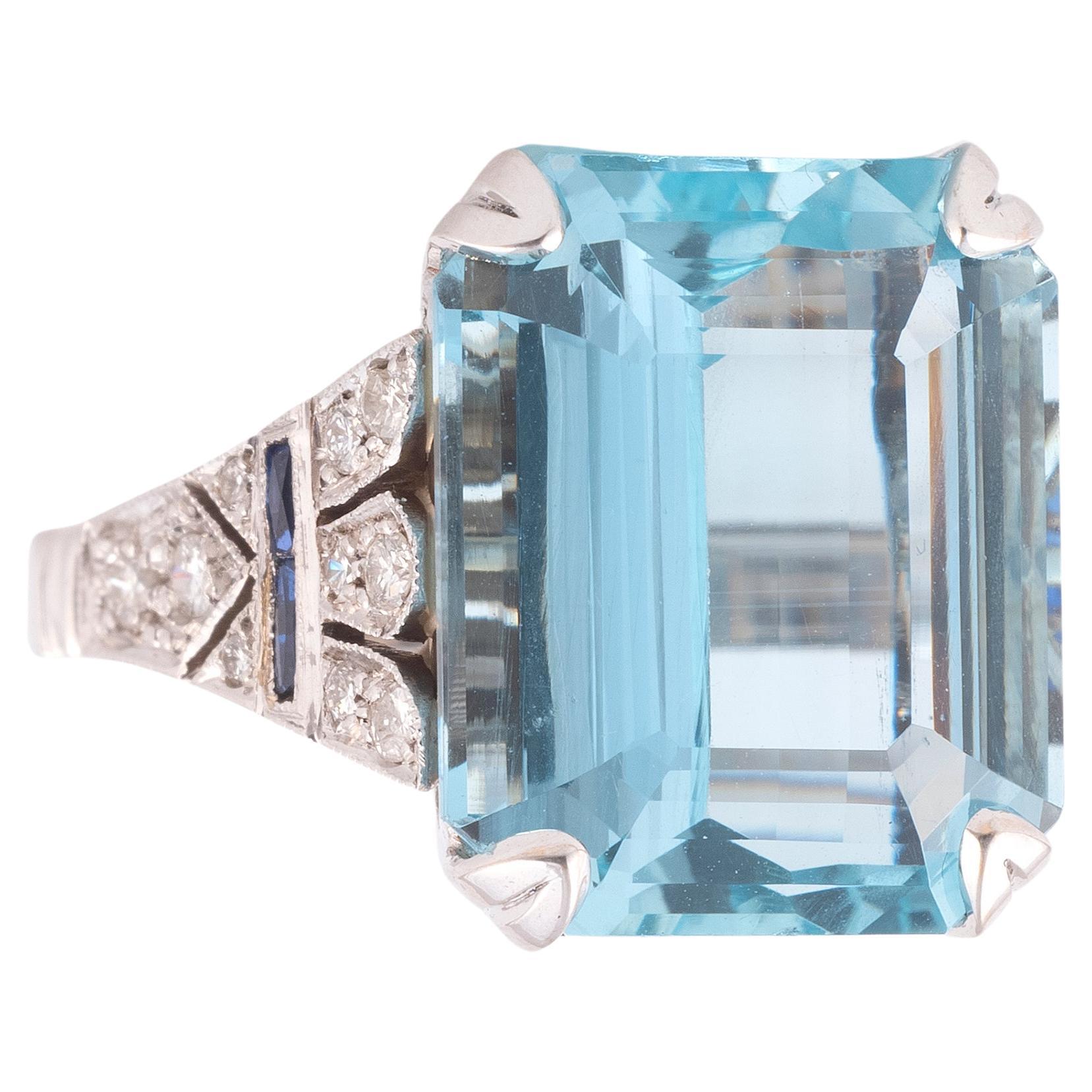 An aquamarine and diamond ring, claw-set with a step-cut aquamarine weighing approximately 15.00 carats, to stepped shoulders set with single-cut diamonds and carré sapphire,mounted in white gold
Size 7 1/4
Weight: 10.52gr.