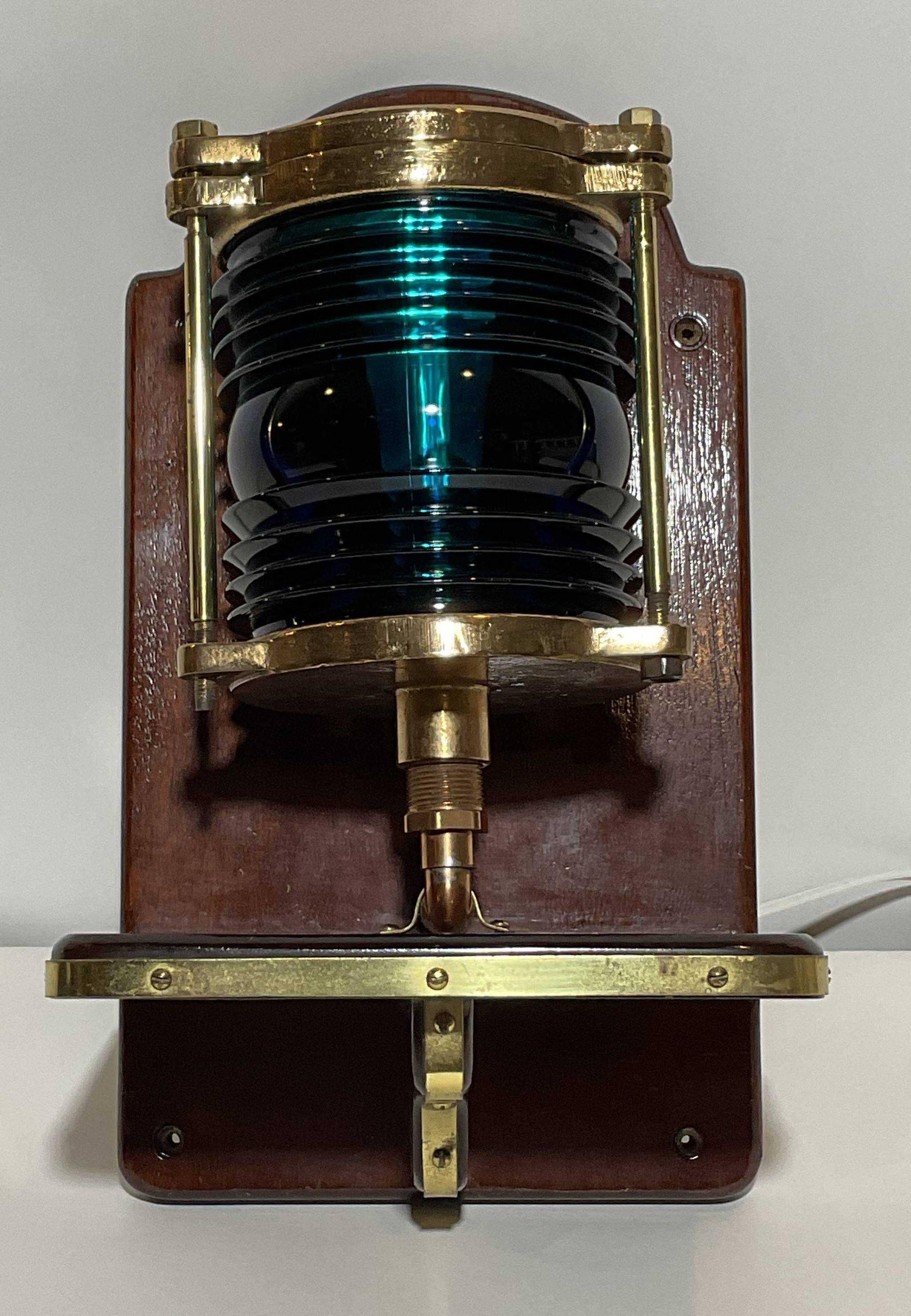 Polished brass nautical beacon with ribbed glass fresnel lens mounted to a brass trimmed mahogany backboard. Electrified. Beautiful color. Light 10x7x7 Base 17x10x8 16 lbs.