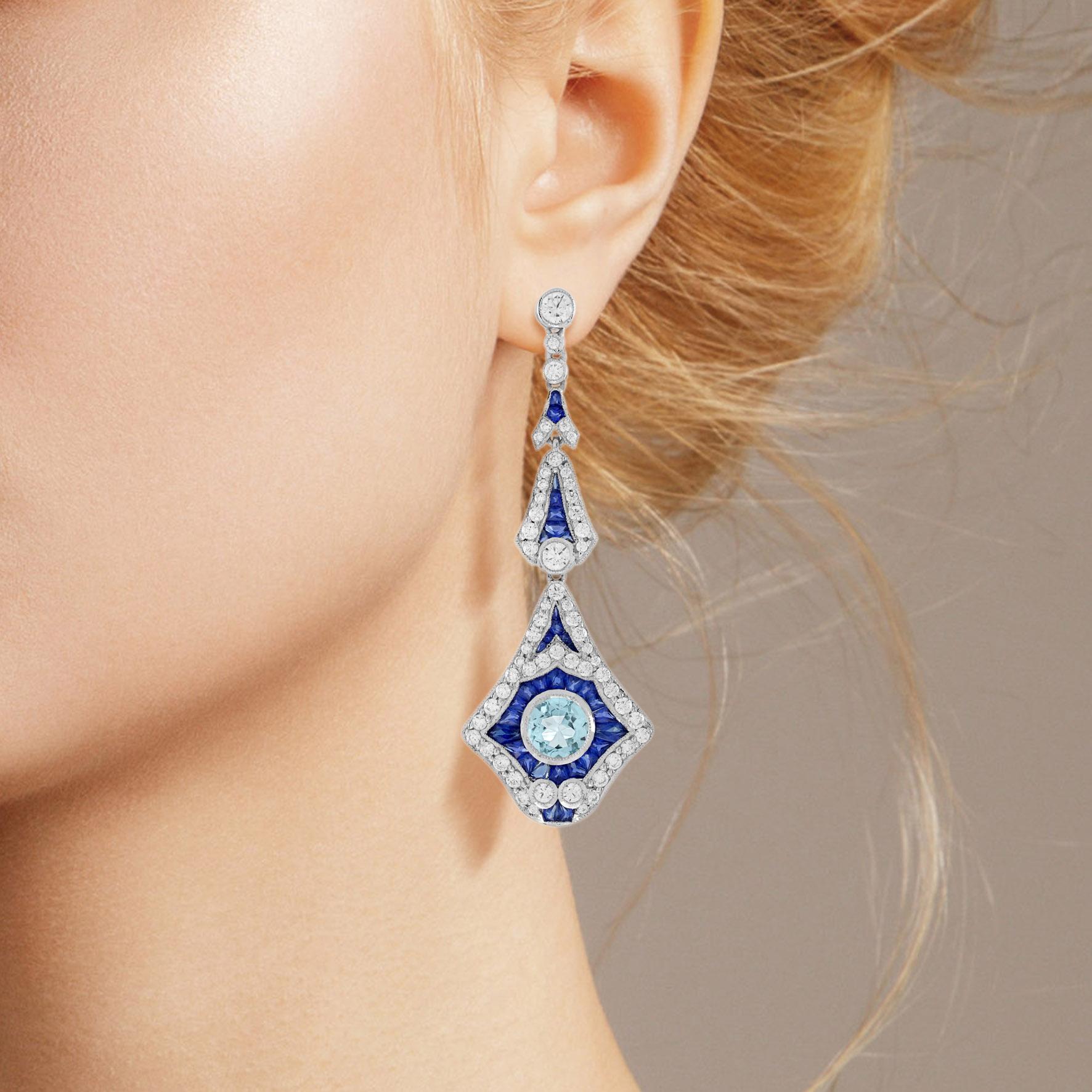 A fabulous pair of Art Deco inspired drop earrings decorated with round aquamarines in their centers, accented with French cut blue sapphires and glittering diamonds. Measuring about 56 mm. long, they are crafted in 18k white gold with fine milgrain