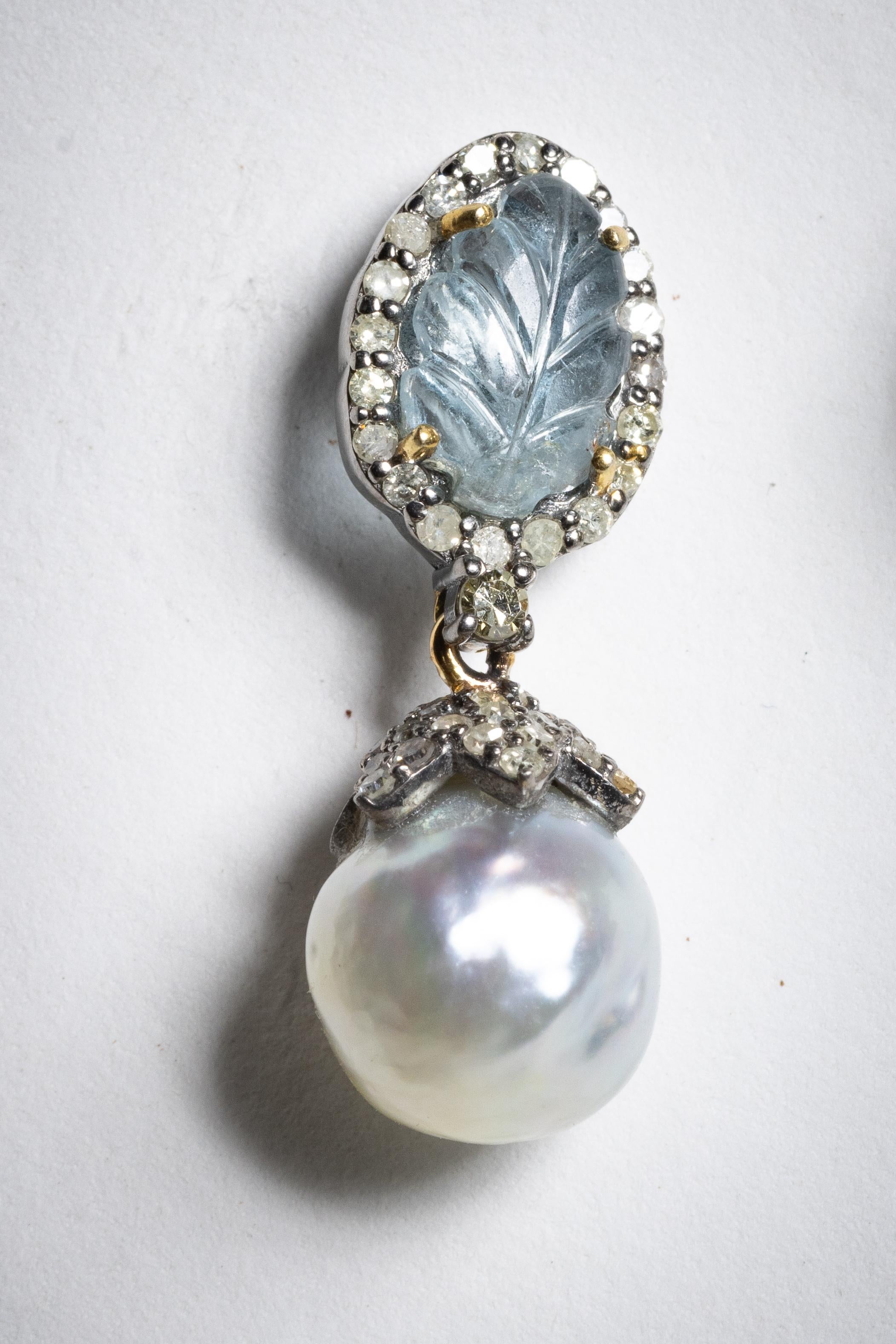 A lovely pair of drop earrings feauring a carved aquamarine at the top in a leaf design which is bordered with round, brilliant cut diamonds.  The end cap over the 12mm silver pearl also has pave`-set diamonds.  Carat weight of aquamarines total