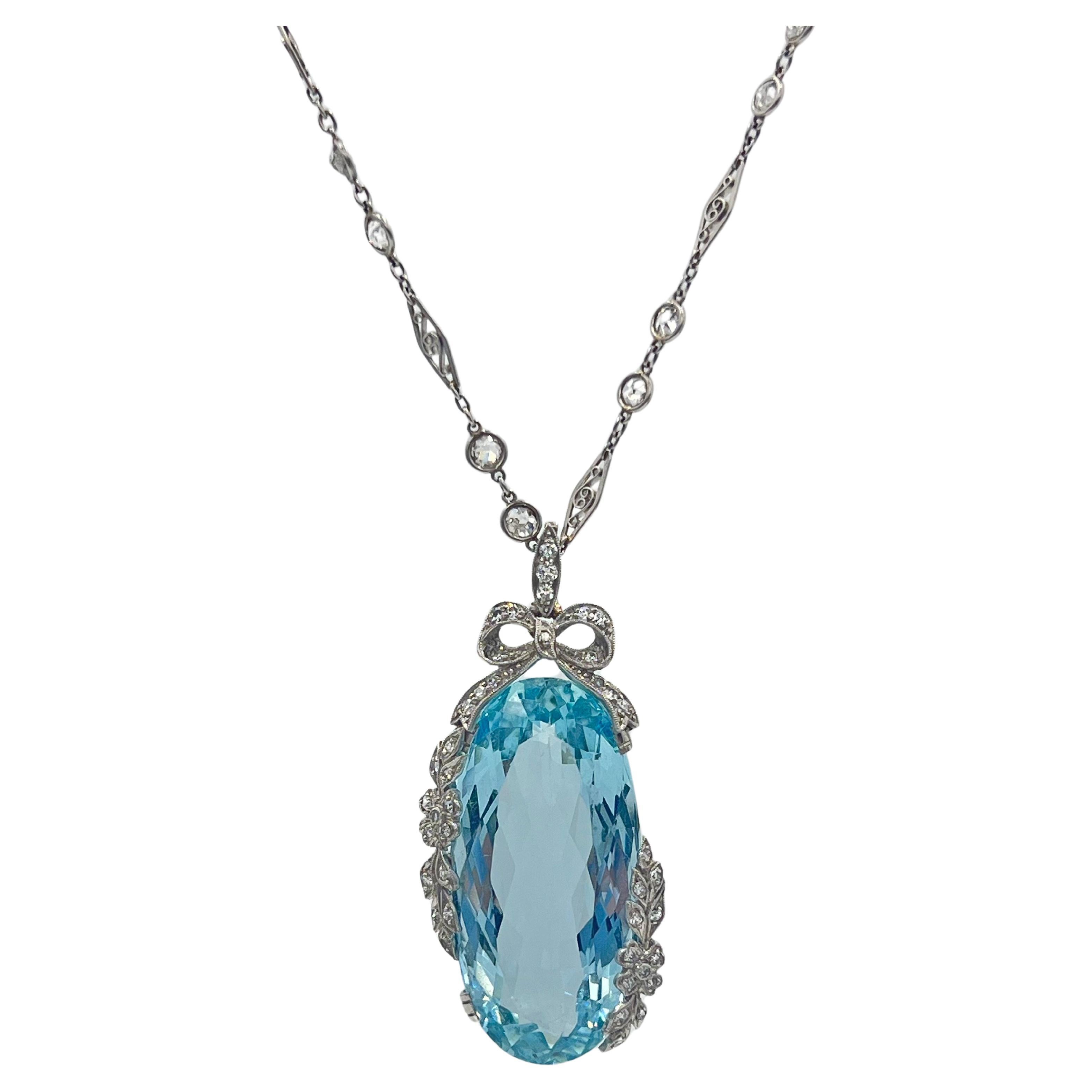 Belle Époque aquamarine and diamond pendant in a handcrafted platinum mounting, featuring an elongated oval-shaped faceted aquamarine weighing over 34 carats with a circular-cut diamond-set bow surmount and circular-cut diamond-set garland leaf