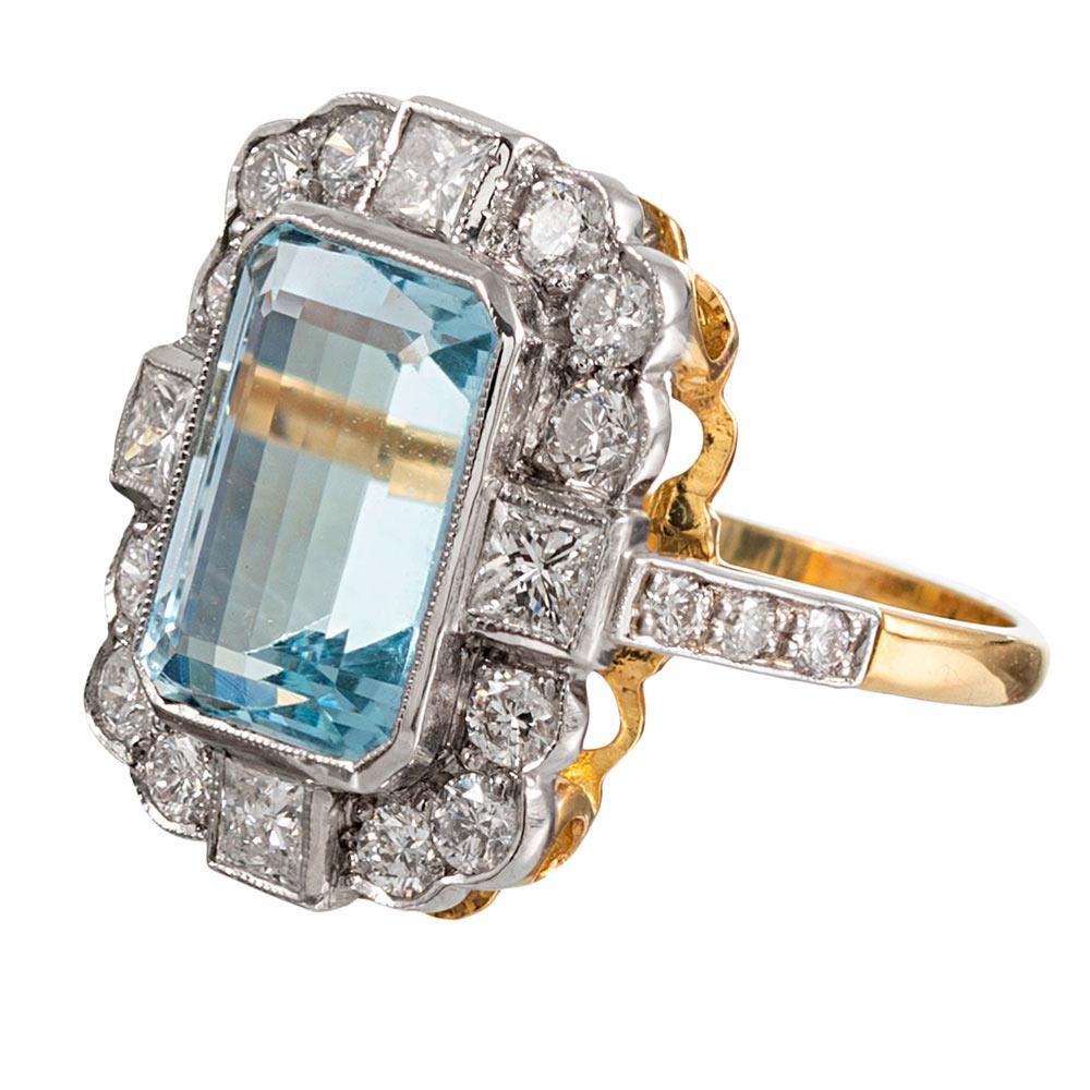 A classically styled cluster centered upon a 4 carat emerald cut aquamarine, the ring is made of 18 karat white & yellow gold and set with 1.30 carats of brilliant round diamonds. The diamonds are set in a scalloped border with stones set in square