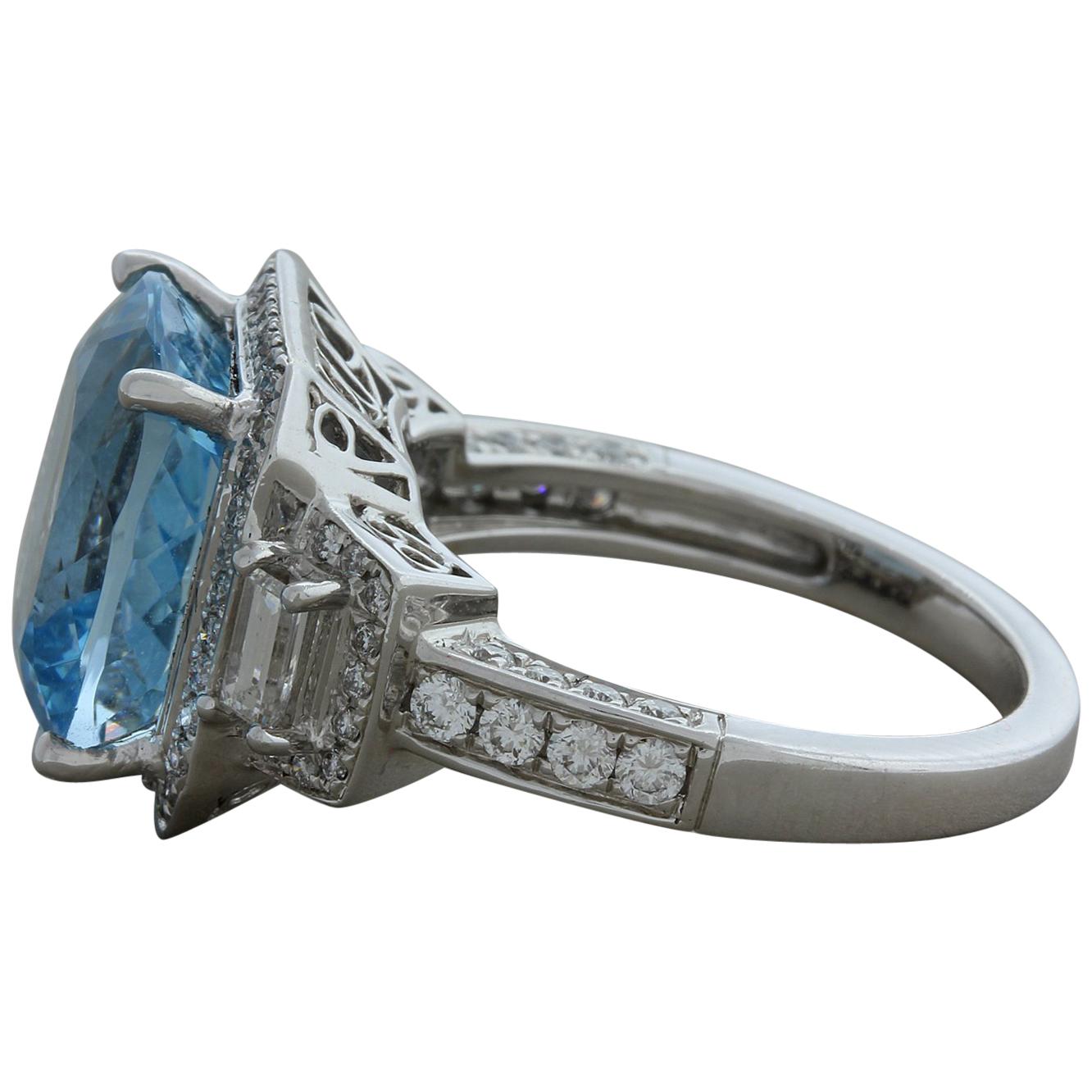 A classic cocktail ring featuring a 6.53 carat cushion cut aquamarine. The soft blue gemstone is accented by a halo of round brilliant cut diamonds as well as two large baguette cut diamonds set on both sides of the ring. There are also round cuts