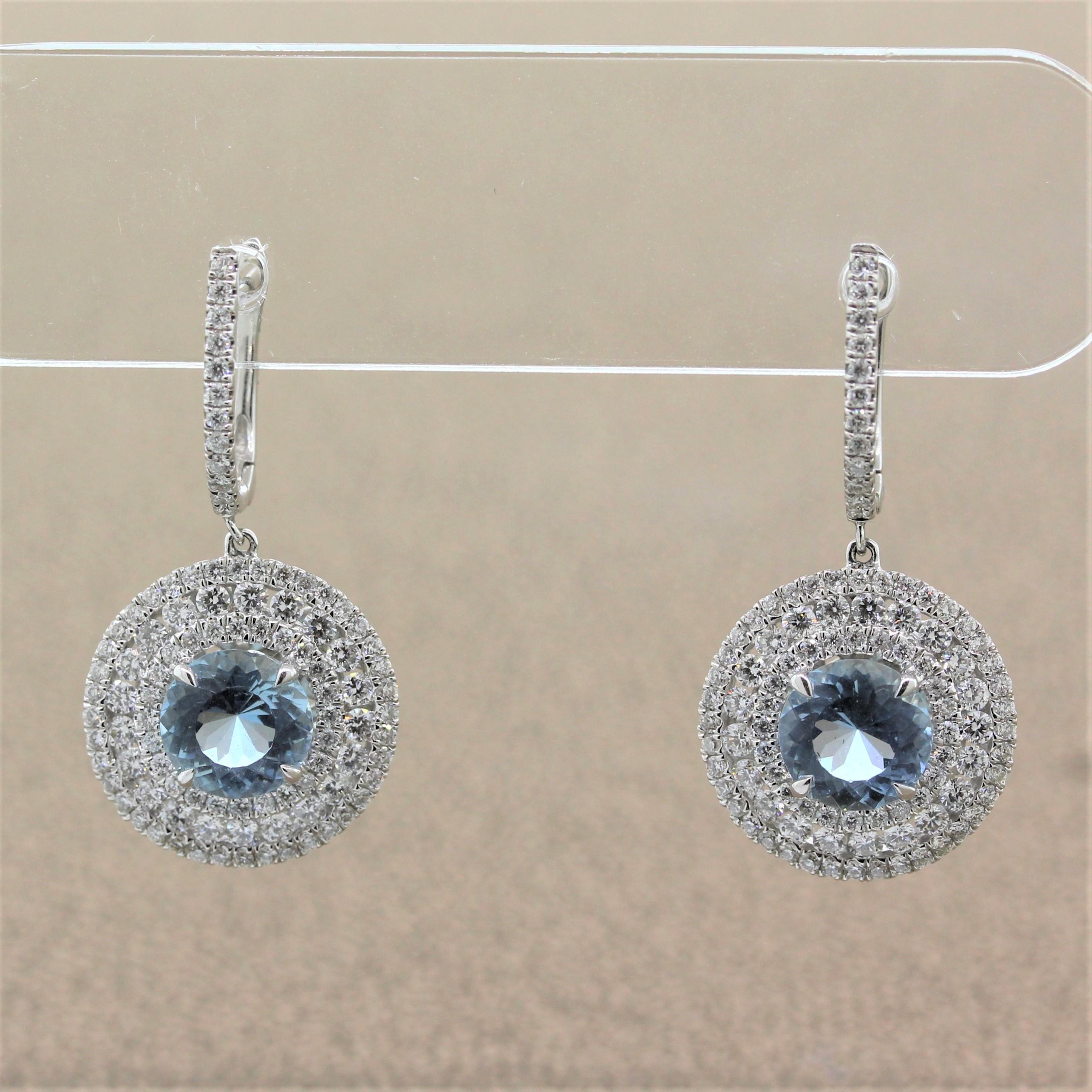 A graceful pair of drop earrings featuring 2.40 carats of aquamarine. The round cut aquamarines are encircled by a triple halo of round cut diamonds weighing 1.90 carats. Each halo of this 18K white gold earring has a different size diamond giving