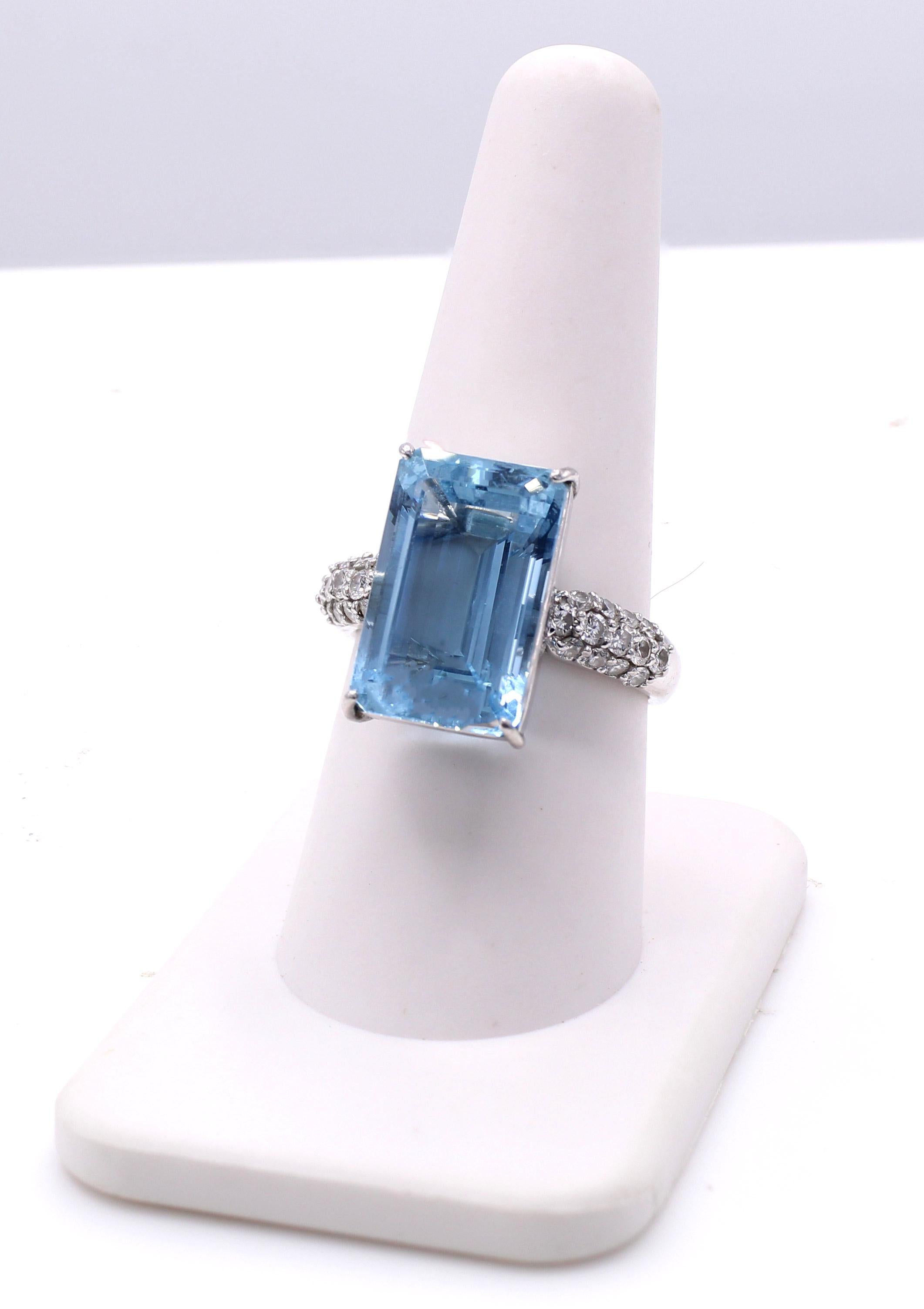 A beautifully cut elongated emerald cut aquamarine weighing 10.67 carats is the center piece of this 1980s platinum cocktail ring. The aquamarine has a wonderful well saturated aqua blue color with wonderful brilliance. The center gem is embellished