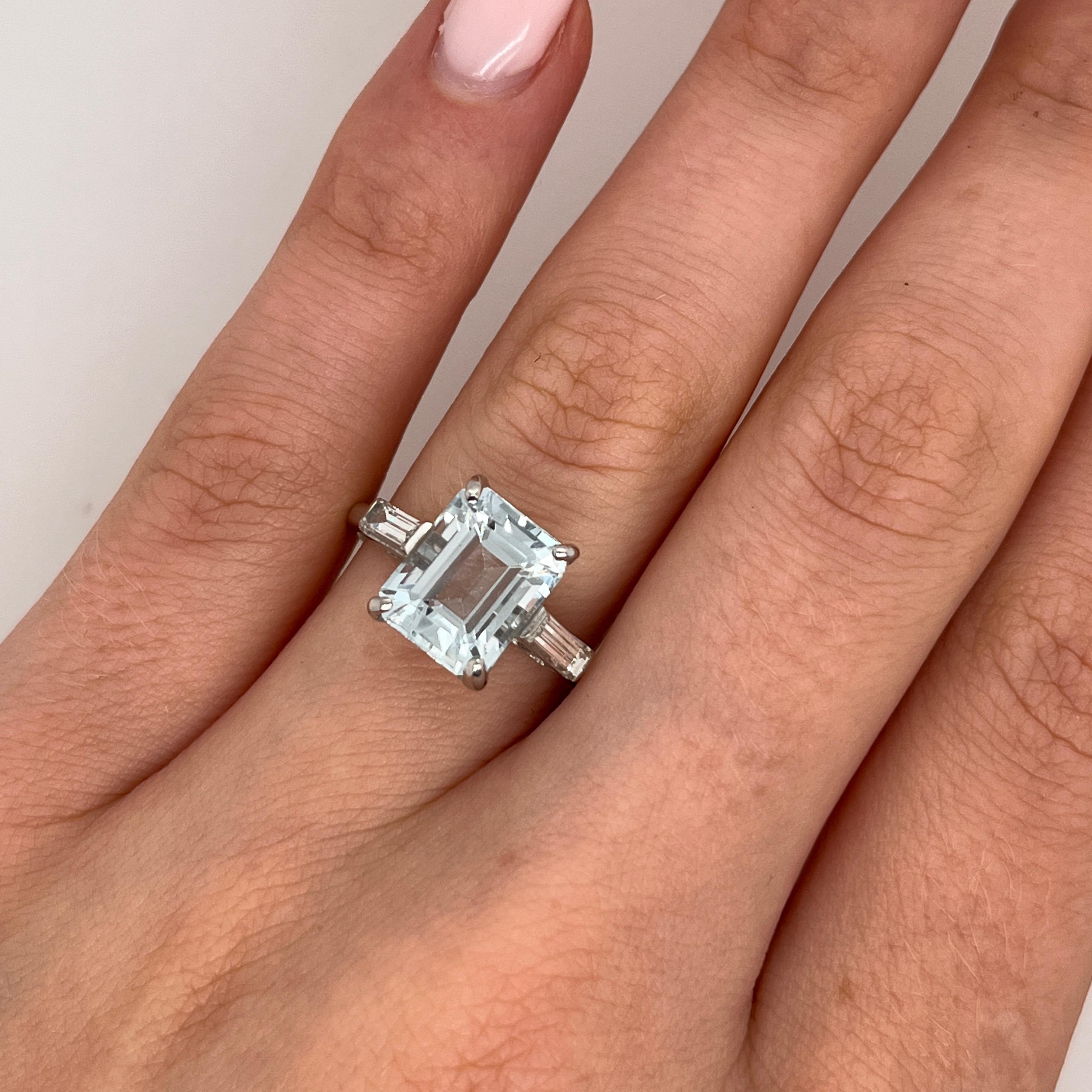 Ein exquisites und zeitloses Design. Dieser elegante Ring präsentiert einen leuchtenden Aquamarin als Herzstück, 
flankiert von zwei passenden Diamanten im Baguetteschliff 
auf den Schultern für einen raffinierten und ausgewogenen Look in Platin