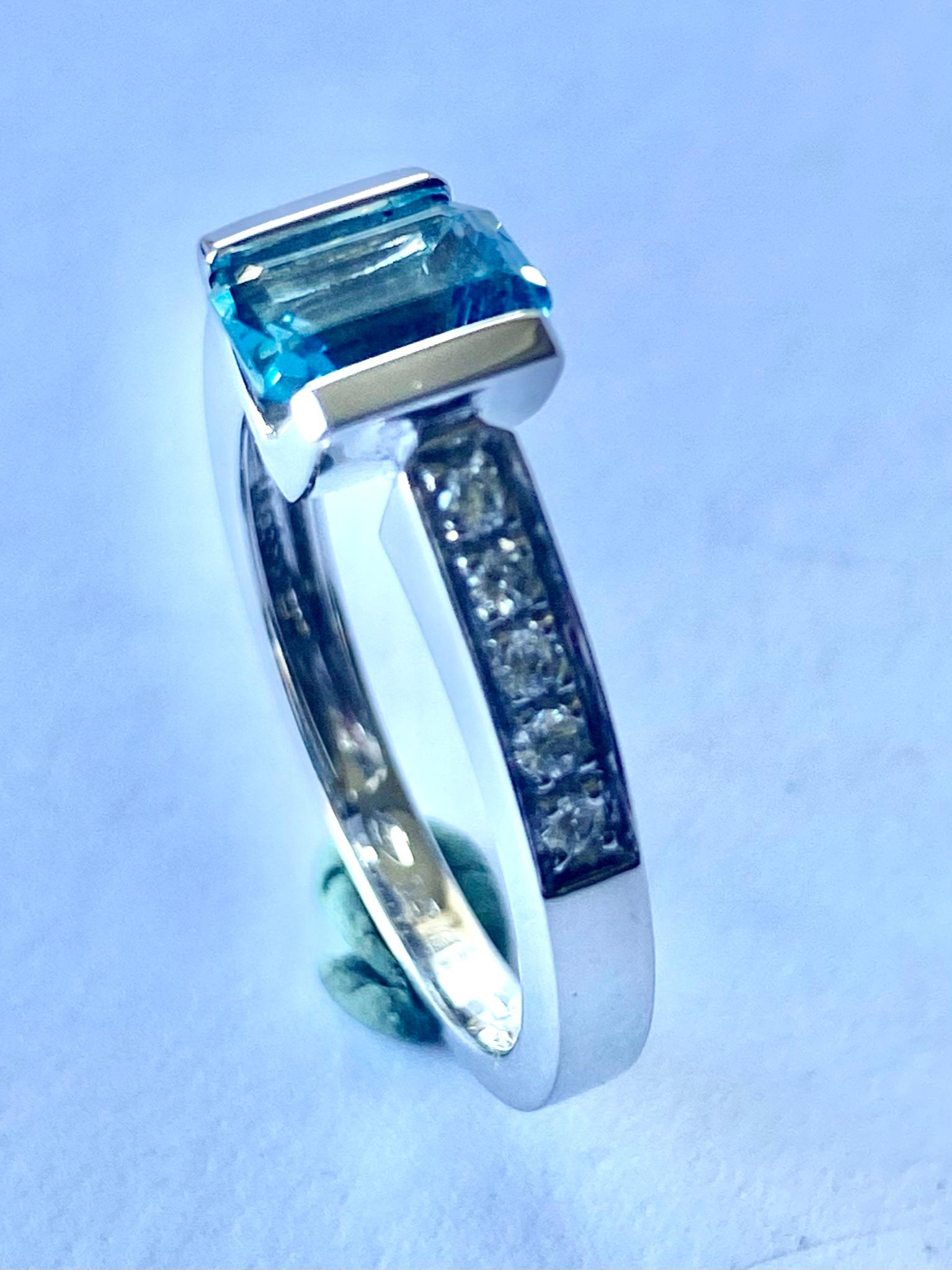 Ein (1) Ring aus 18 Karat Weißgold, gestempelt: 750 und  *3231 AL = Alberti  Gioielli Valenza Italien.
Ein natürlicher Aquamarin, Smaragdschliff = 0,95 ct.  (Farbe Hellblau)
Zehn (10) runde Diamanten im Brillantschliff acht: 0,18 ct.  VS  F-G