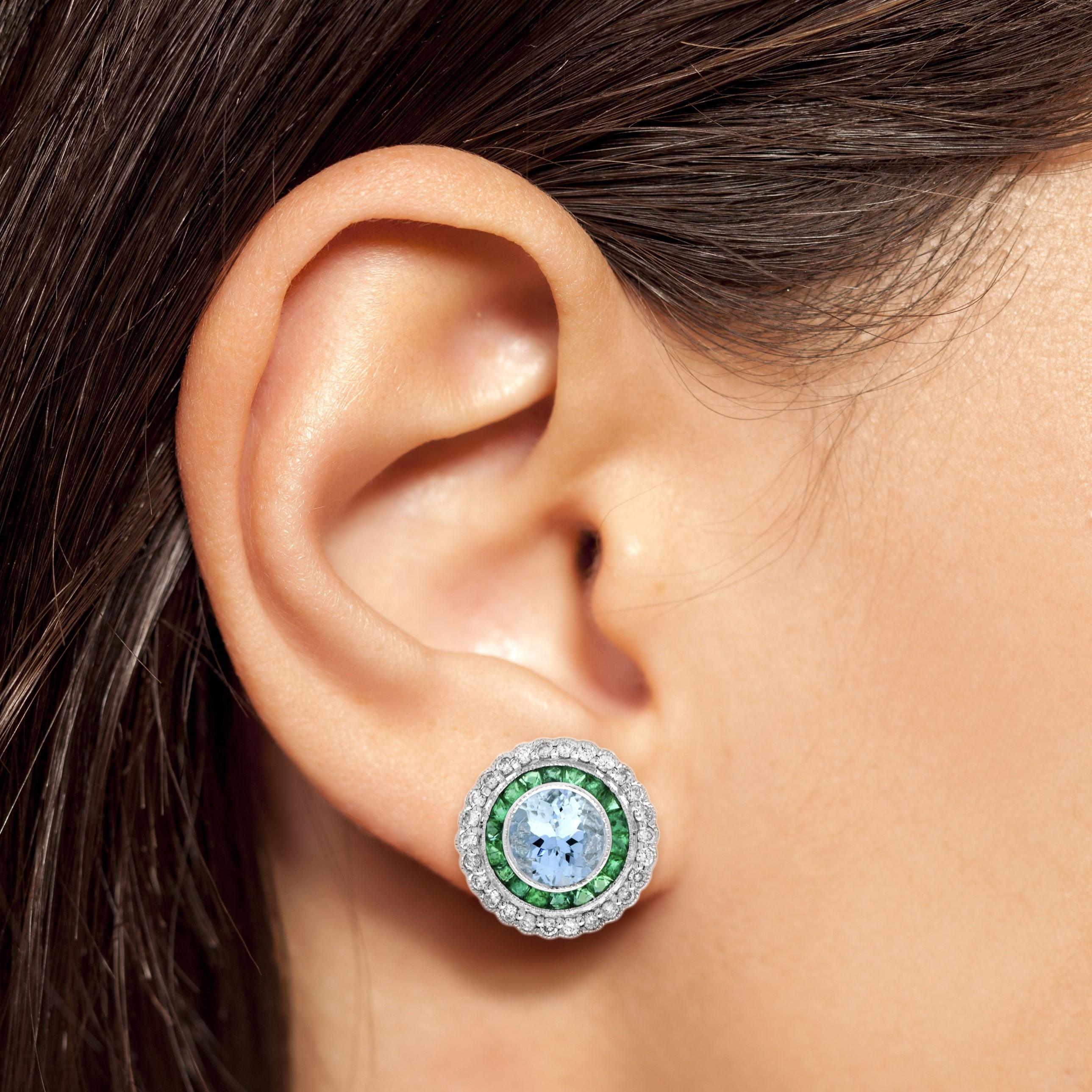 This Art-Deco stud earrings are completely spectacular! The vibrant green color stone of emerald are specialty cut to surround the excellent center aquamarine, which is in a thin bezel with mil-grain detail. Crafted in 18k white gold.

Earrings