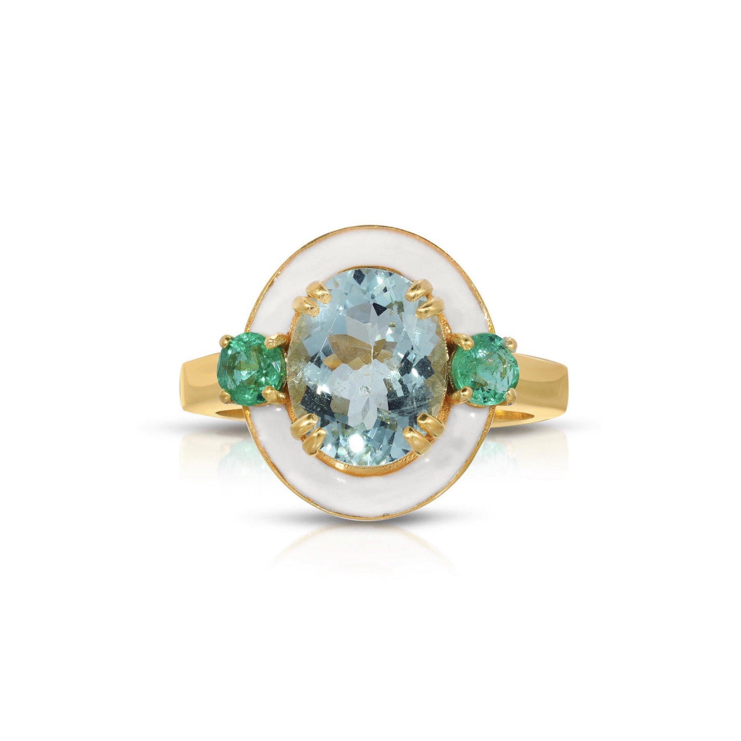 A beautiful cocktail ring of modern design with a mix of gorgeous gemstones and enamel. This ring features a beautiful, oval cut Icy Blue Aquamarine center stone set with two round cut fiery Emeralds and glossy white enamel. This ring is set in