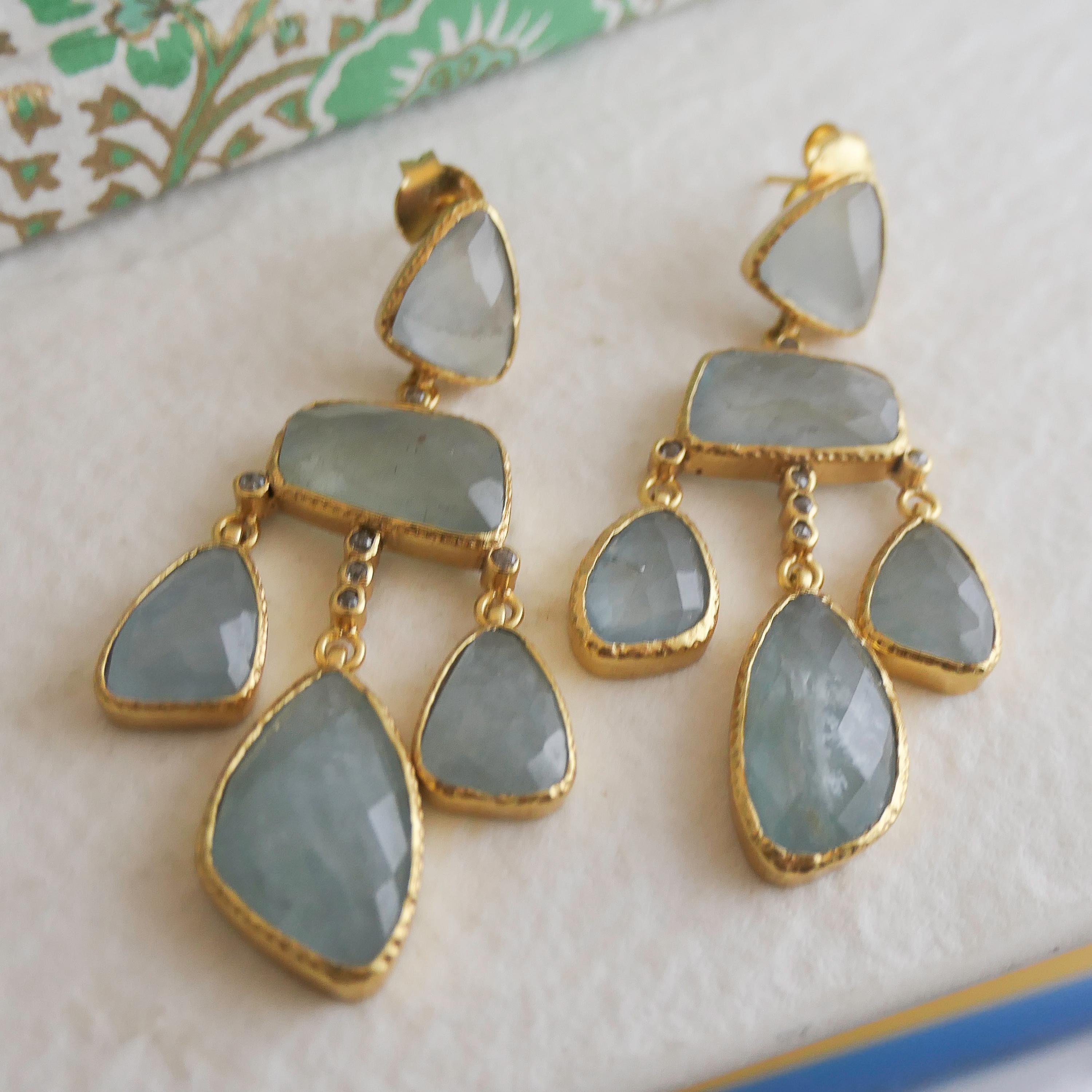 Eleganti e accattivanti, questi orecchini a lampadario fatti a mano sono caratterizzati da splendide gemme di acquamarina sfaccettate in morbide tonalità blu ghiaccio. Ciascuna pietra è incastonata in argento sterling placcato oro con una texture