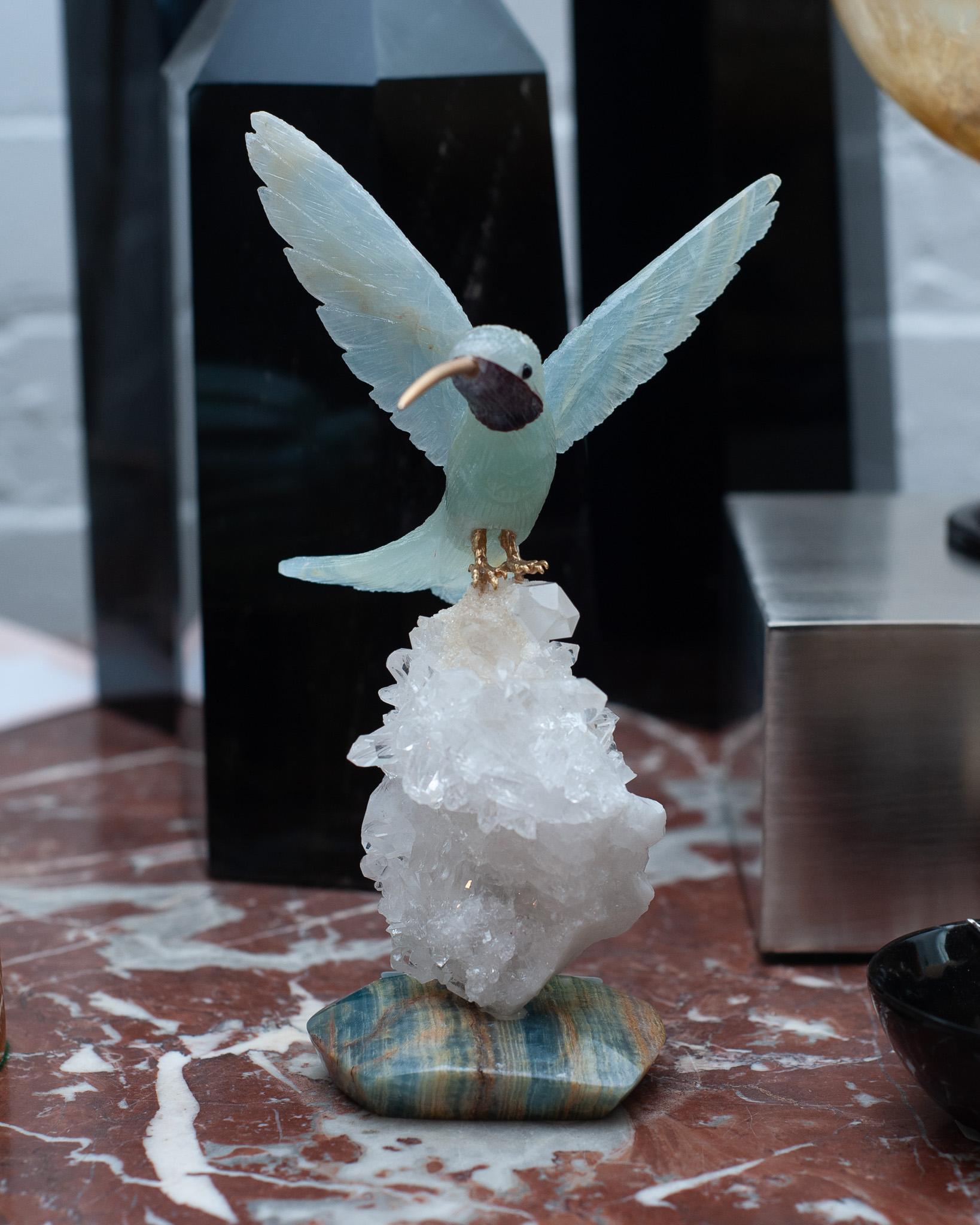 A beautiful hand carved semi precious aquamarine stone hummingbird sculpture with brass beak and legs, mounted on a rock crystal quartz and blue onyx mineral specimen base. This exotic bird is a decorative combination of ornithology and geology.